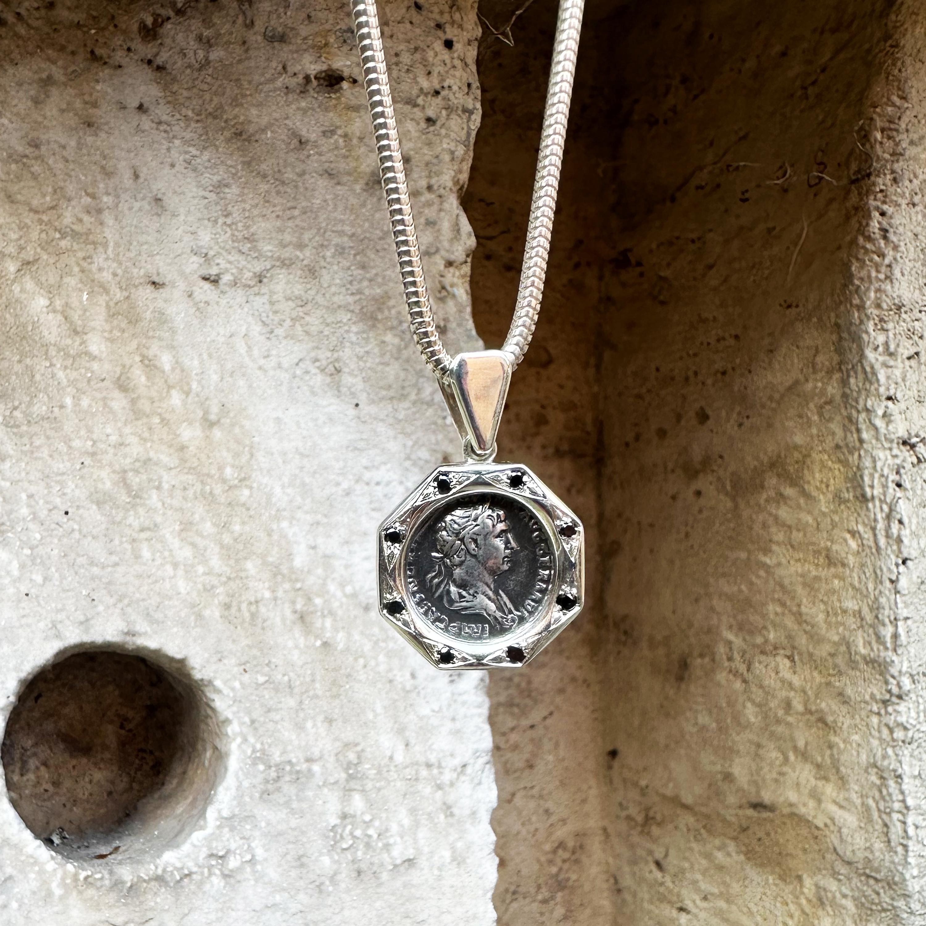 This exquisite silver pendant showcases a genuine Roman silver denarius coin dating back to the 2nd century AD, depicting Emperor Trajan on its front and God Mars on the reverse. Accentuating its allure, the pendant is embellished with 8 black