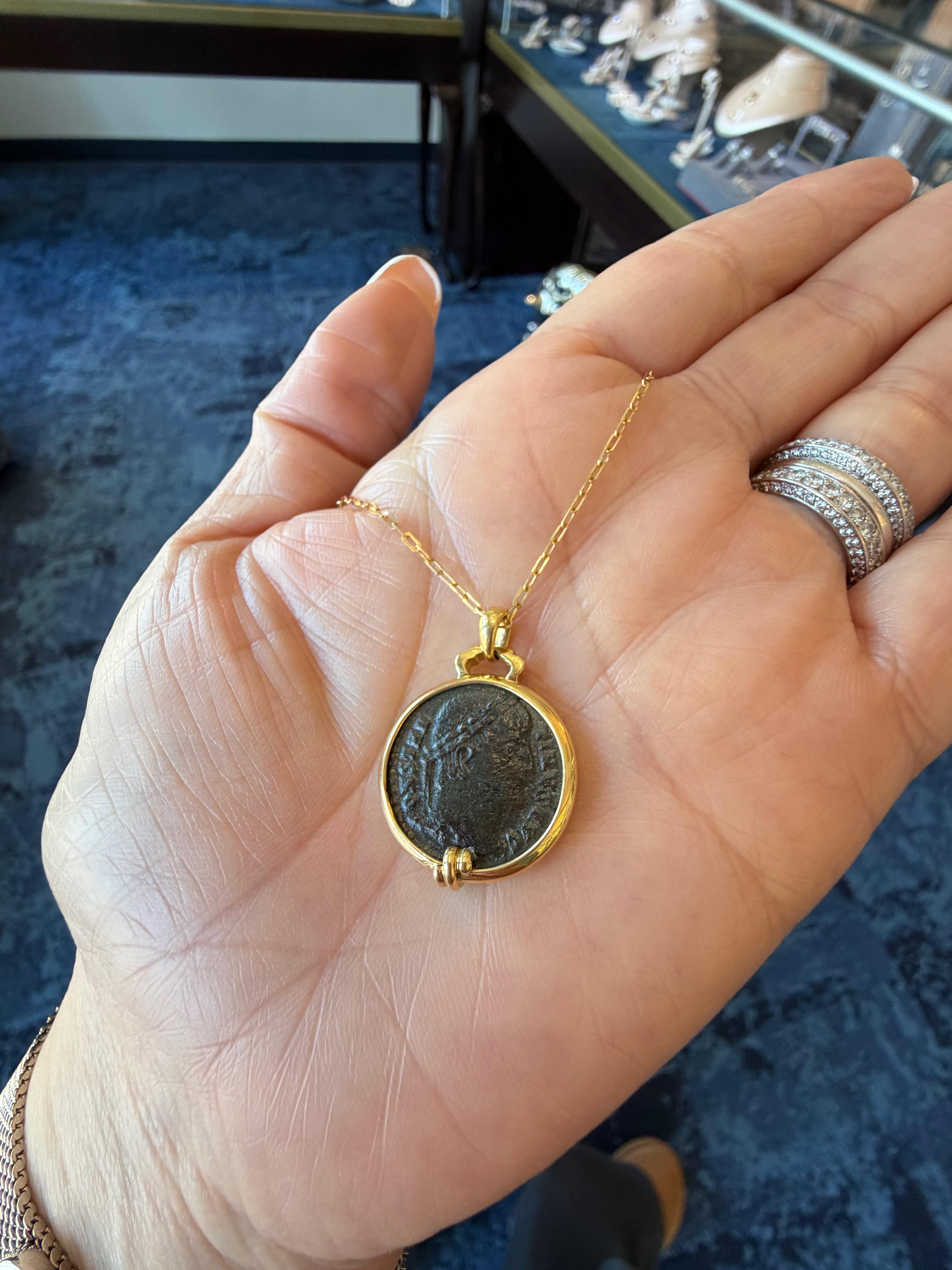Ce collier en or jaune 18 carats présente une pièce de monnaie romaine authentique de Constantin I+I, élégamment encadrée dans une monture polie. Un anneau d'inspiration vintage ajoute du caractère, tandis qu'un gracieux motif enveloppant orne le