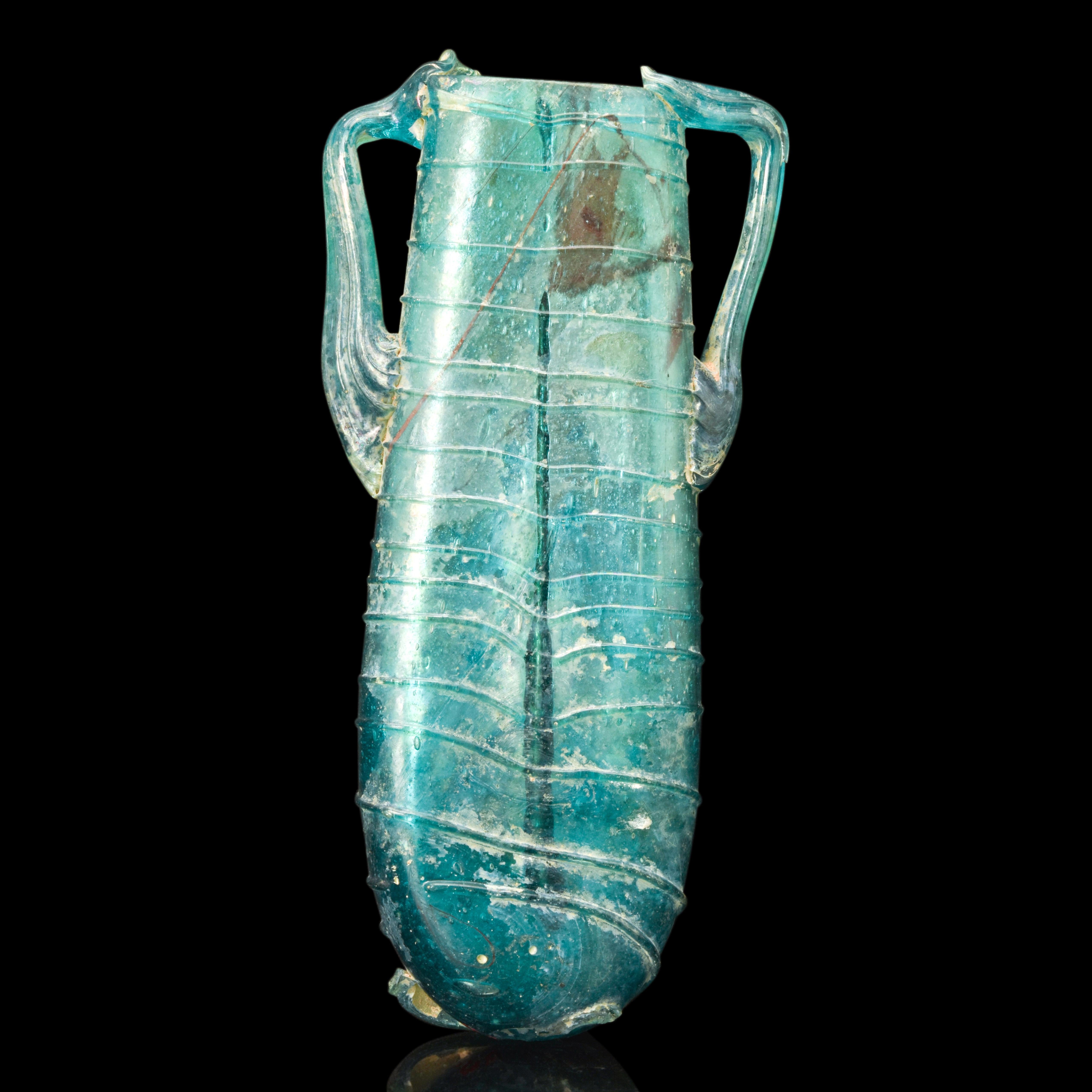 A Roman double balsamarium made of translucent, bright blue-green glass. The vessel is composed of two tubular phials, rims folded inward and bulging slightly in the middle. Both phials have a delicate glass thread carefully wrapped around the