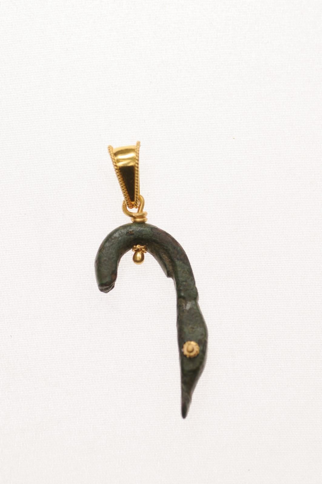 Un'affascinante testa di anatra in bronzo dell'Antico Impero Romano trasformata in un ciondolo rifinito con accenti e balla in oro 21 carati. Una meravigliosa patina dimostra l'età del frammento. È datato approssimativamente tra il I e il III secolo