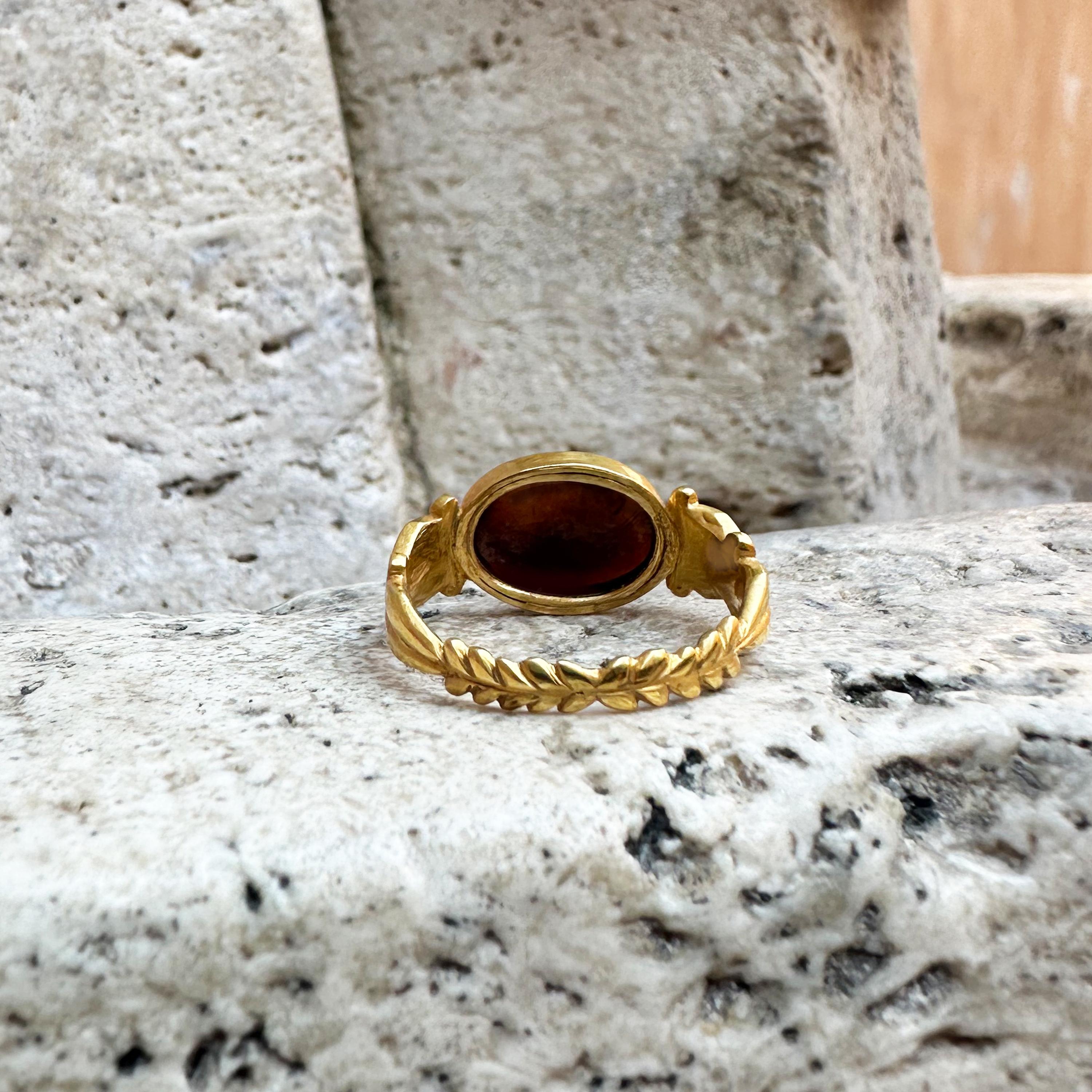 This exquisite 18 kt gold ring showcases a remarkable Roman intaglio on garnet, which dates back to the 1st-2nd century AD. The intaglio depicts the Greek God Apollo, a multifaceted deity in Greek mythology, associated with many aspects of