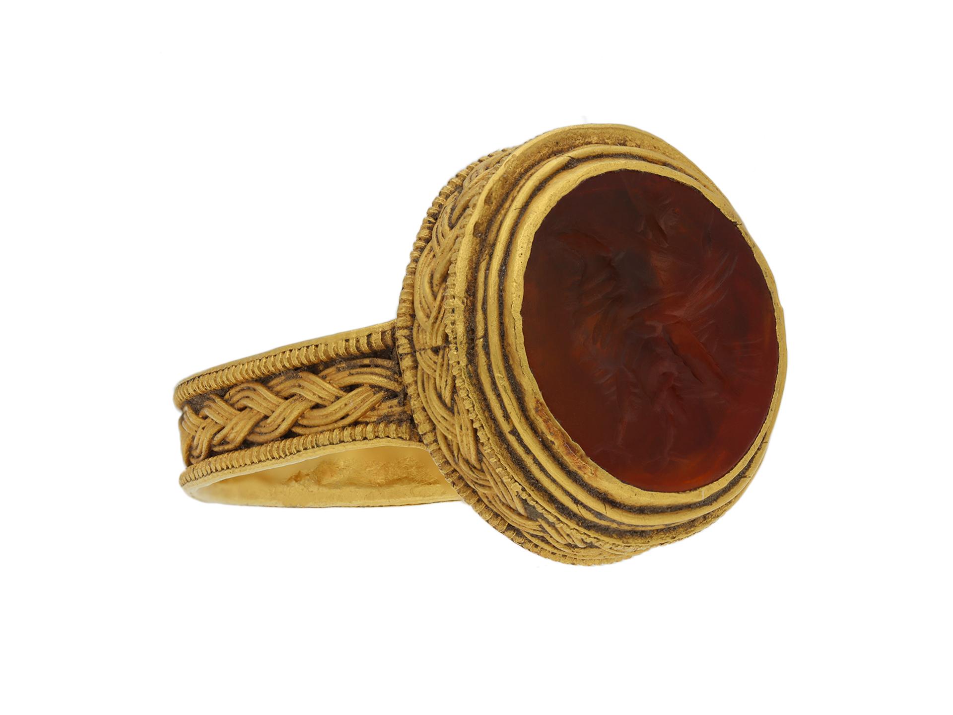 Roman gold finger ring with eagle intaglio. Set with an impressive oval cornelian intaglio of an eagle with outstretched wings in a fine closed back Roman set setting with intricate threaded wirework and granulated borders, continuing down the flat