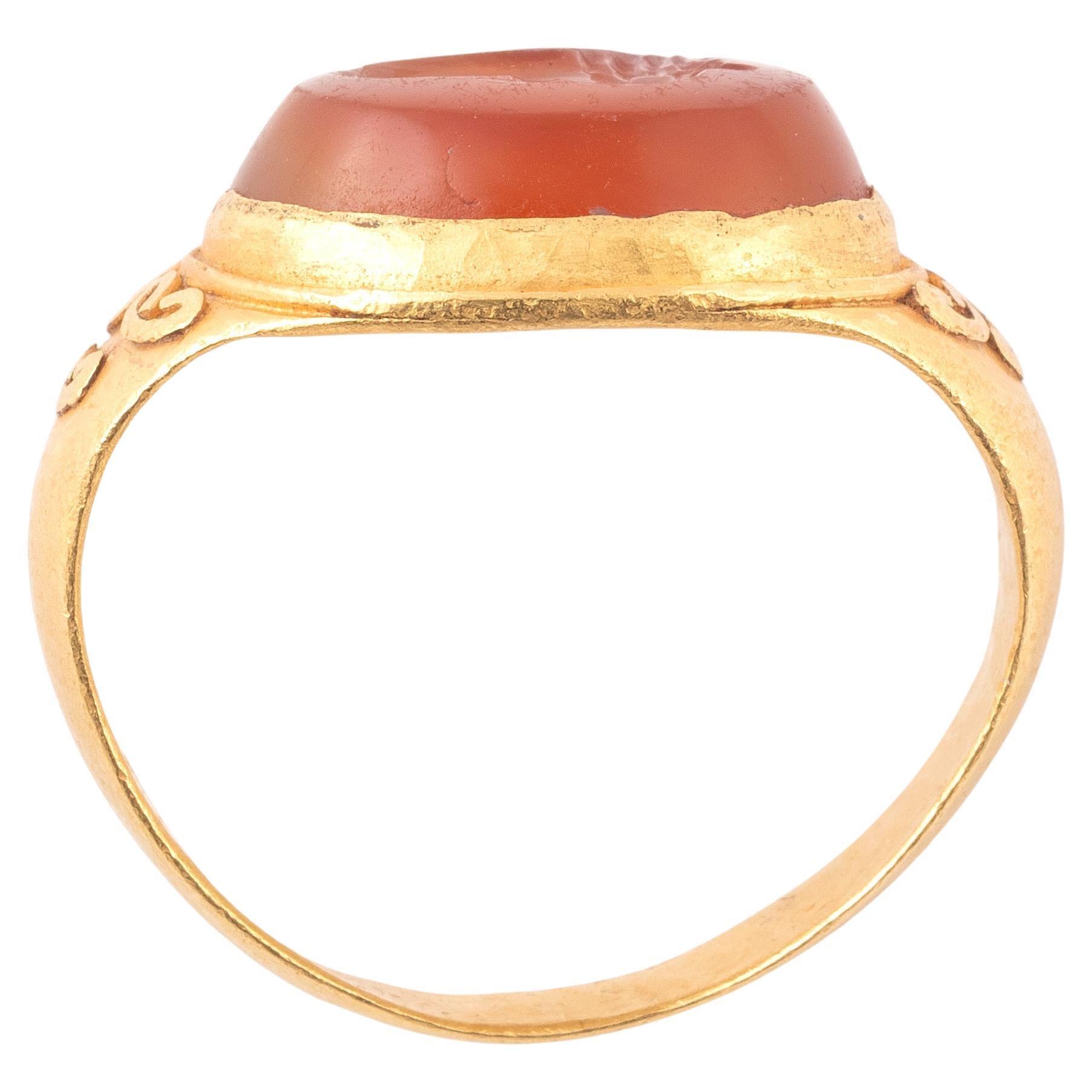 A fine Ancient Roman gold ring featuring a thick gold D-section loop attached to a circular raised bezel. The carnelian inset is framed in gold and has been carefully carved with a gryllos, a combination of an eagle and man. The sileno facing left;