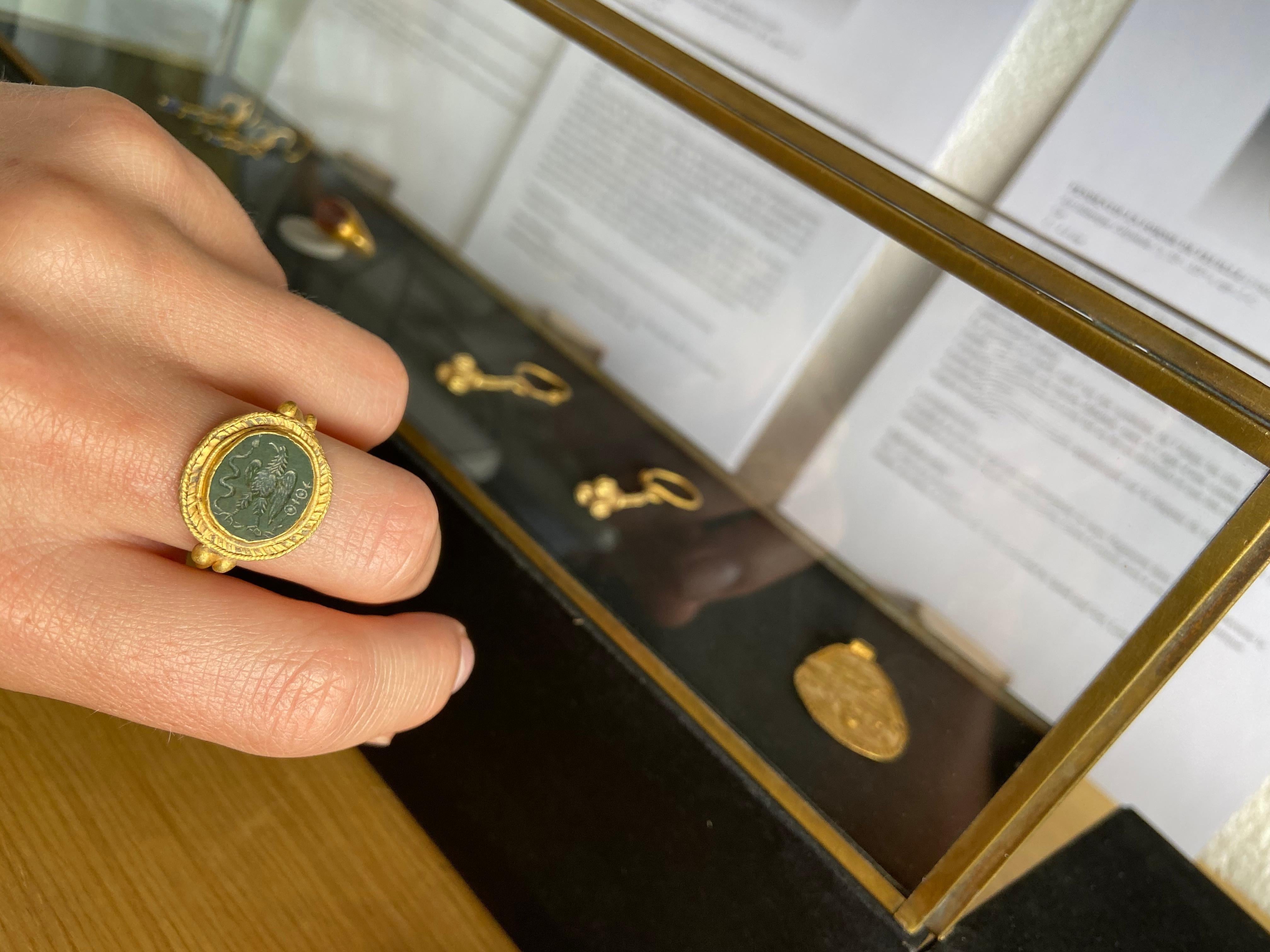 A gold finger ring with granules to the shoulders, disc plaque with applied filigree collar, cell with inset green jasper cloison, intaglio eagle gripping a serpent, military standard to the rear. 5.72 grams, 23.10mm overall, 19.54mm internal