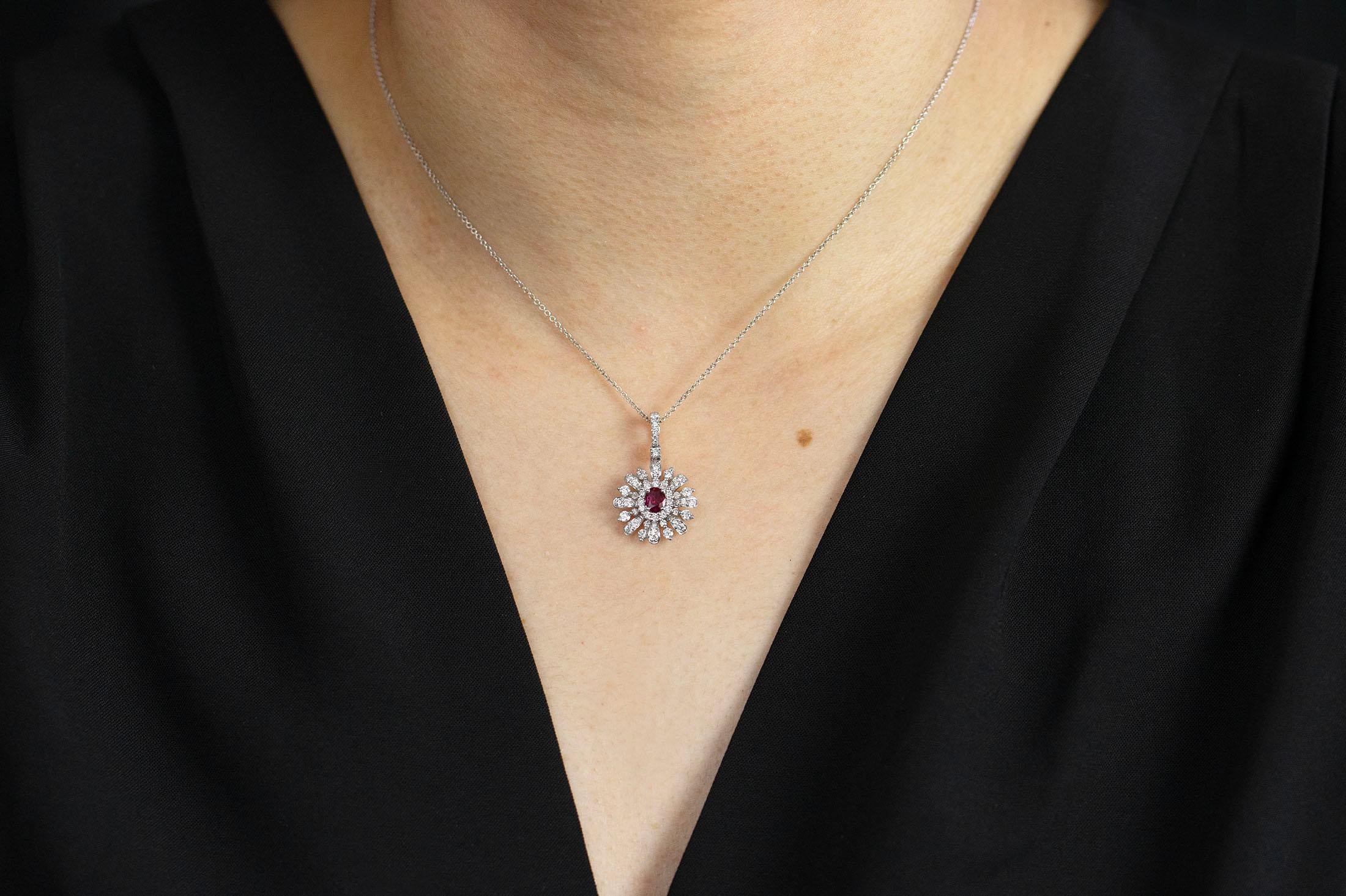 A fashionable and beautiful piece of jewelry showcasing a 0.32 carats color-rich oval cut ruby, set in an intricately sunburst design accented with brilliant round diamonds. Diamonds weigh 0.81 carats total. Made in 18K white gold and suspended on