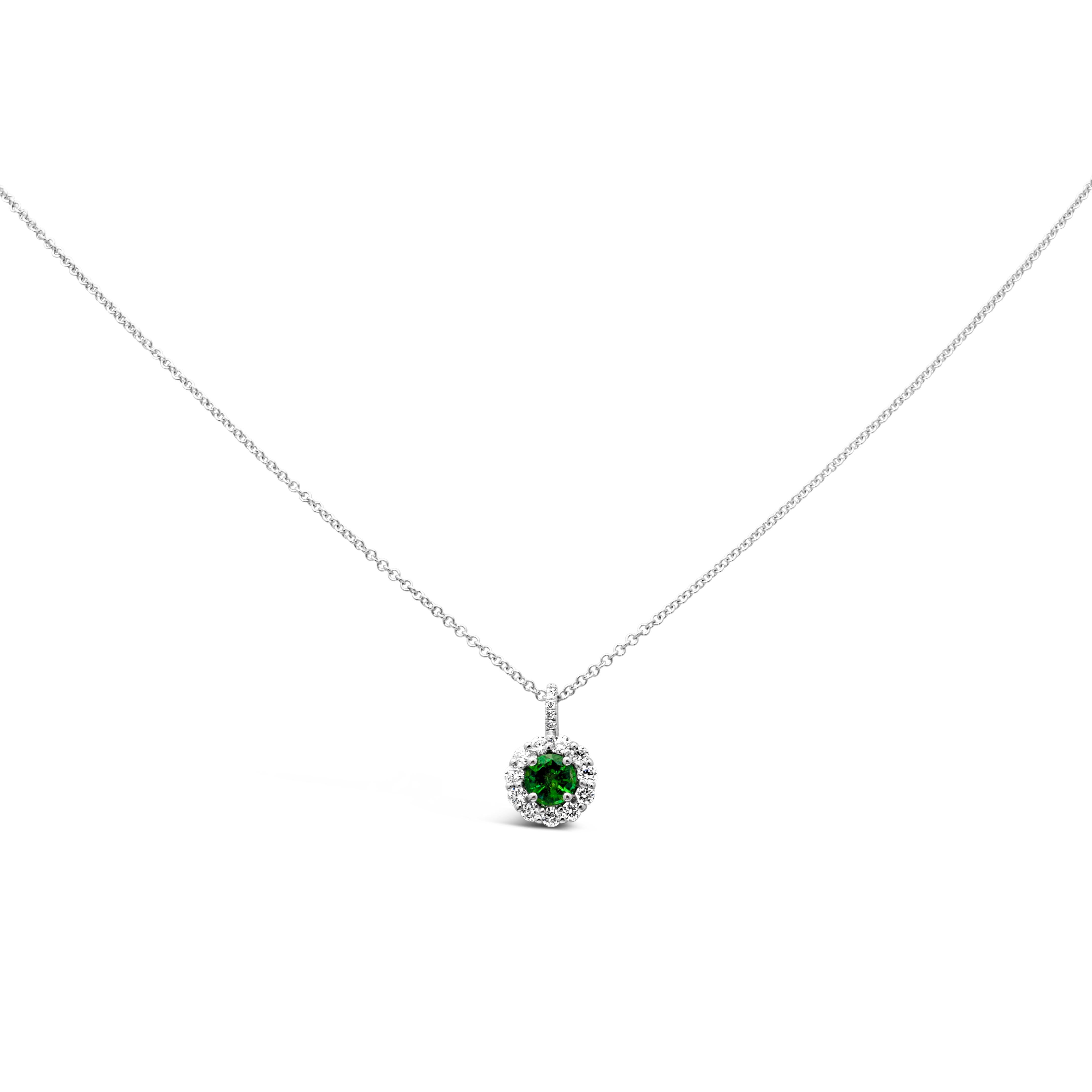 A classy pendant necklace showcasing a brilliant round cut color-rich green emerald weighing 0.33 carats, set in a classic four prong basket setting. Surrounded by a single row of round brilliant diamonds in a halo design weighing 0.25 carats total.