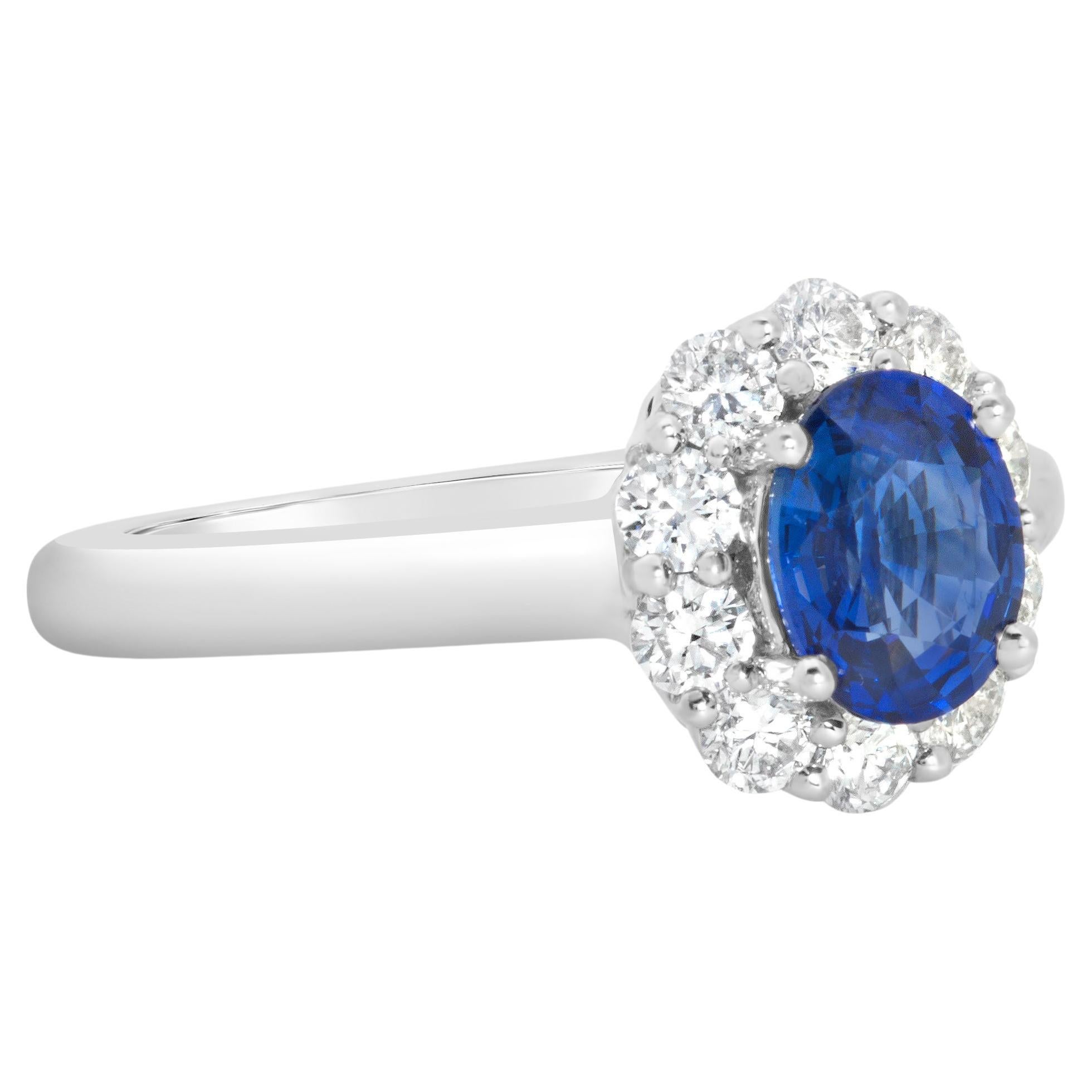 A beautiful engagement ring, showcasing a 0.94 carat oval cut sapphire, set on four rounded prongs. Accented by a halo of round brilliant cut diamonds weighing 0.48 carat total, set on a shared prong setting. Finely made with an 18K white gold