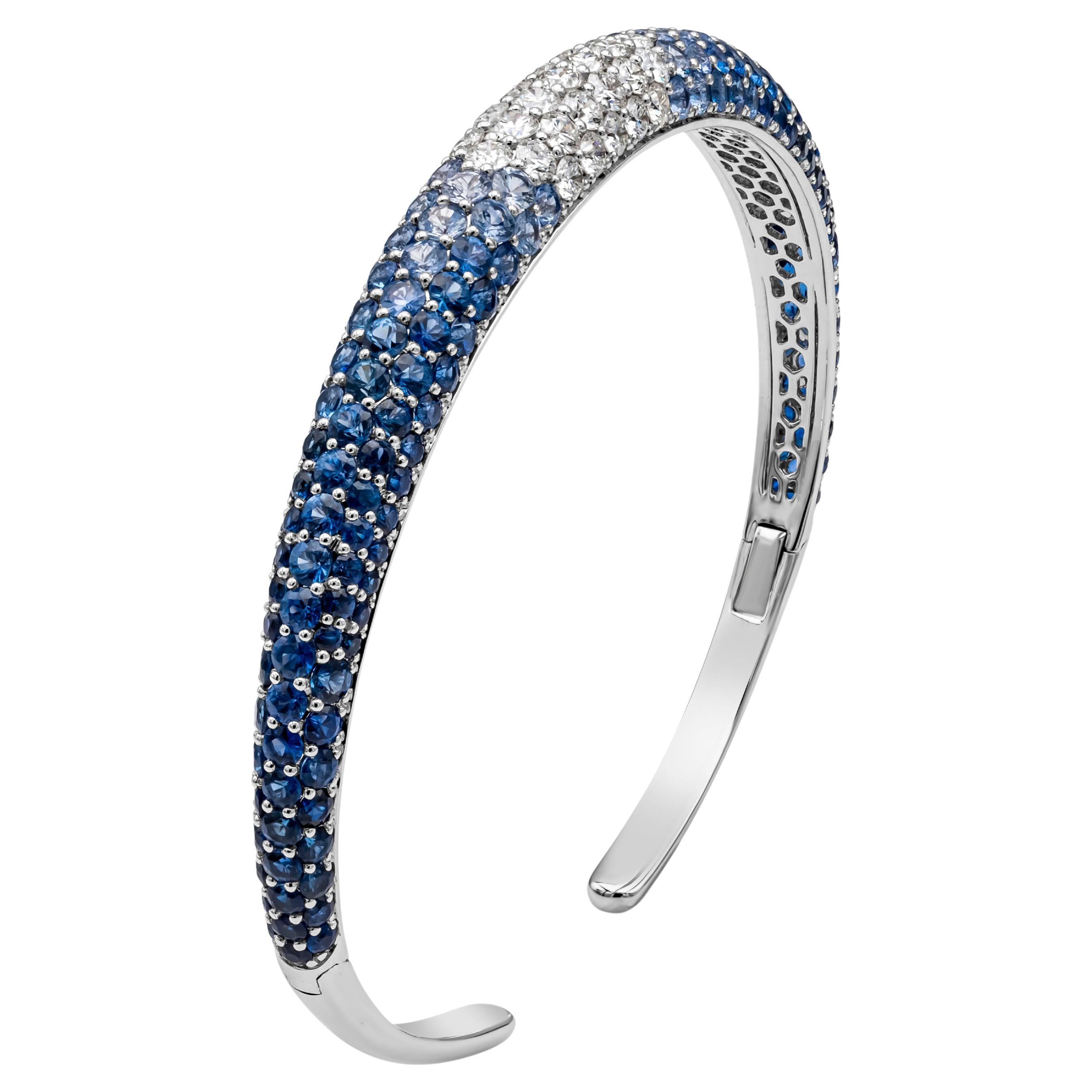 A fashionable and beautiful bangle bracelet, showcasing color-rich round brilliant cut blue sapphires and white diamonds weighing 10.05 carats total. Set on a shared-prong micropavé dome finely made with 18K white gold. Diamonds are approximately