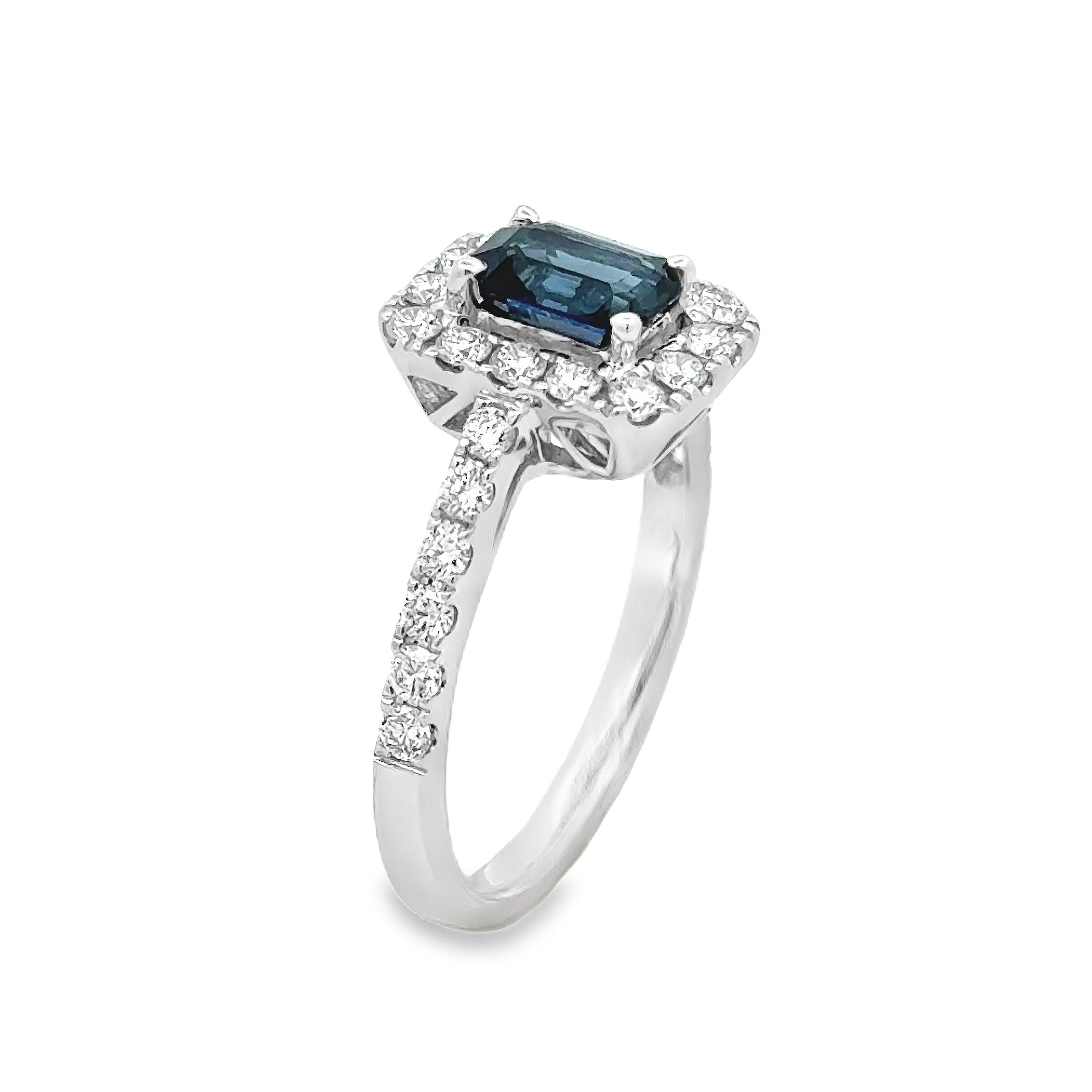 Uno squisito anello di fidanzamento con uno zaffiro taglio smeraldo da 1,03 carati, incastonato in una classica montatura a quattro punte. Circondato da un'aureola di diamanti rotondi taglio brillante e accentuato da un gambo tempestato di diamanti