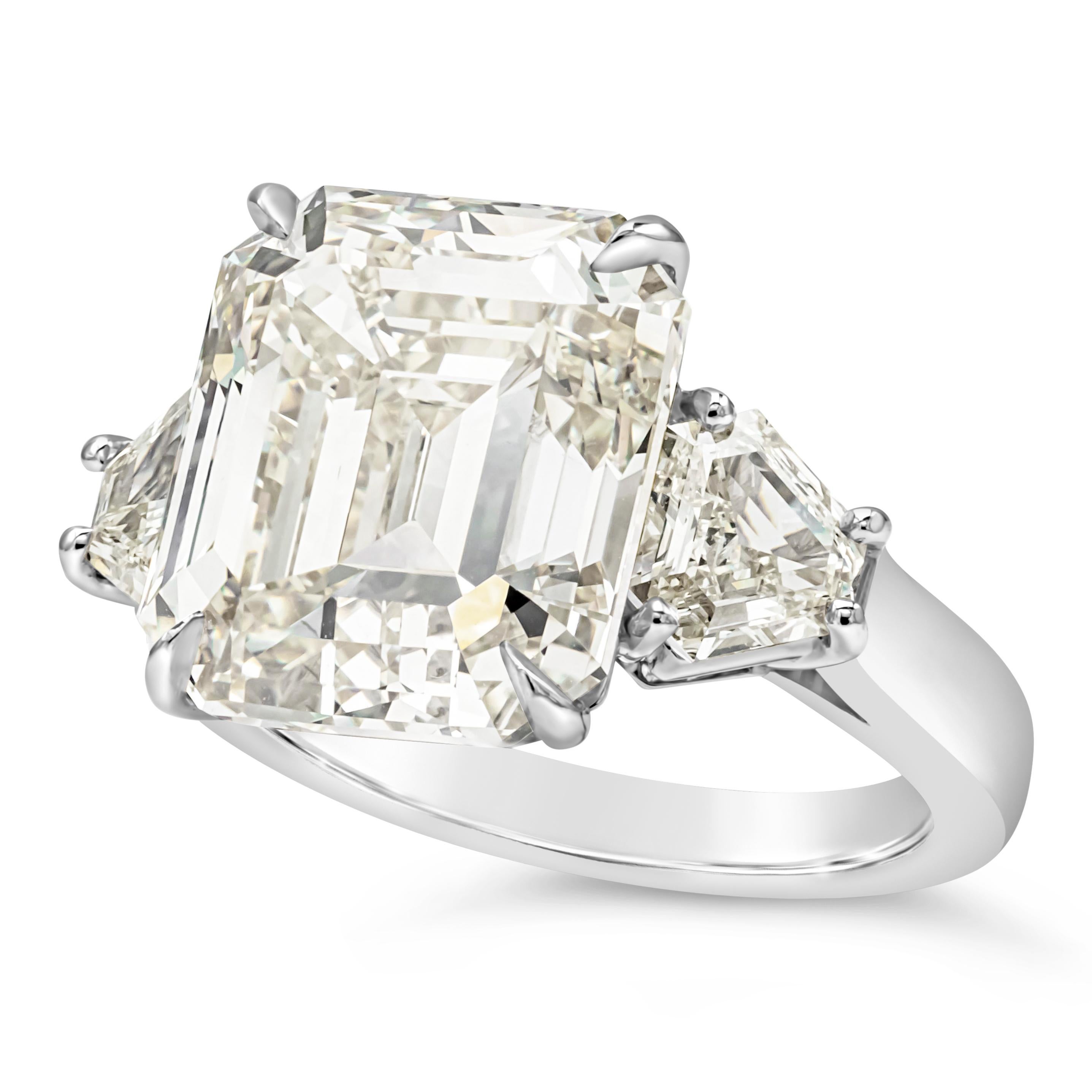 Elegantly made three stone engagement ring features a 11.11 carats emerald cut diamond certified by IGI as M color, VS1 in clarity, set in platinum four prong setting. Flanked by shield step-cut diamonds on each side, weighing 1.11 carats total, M