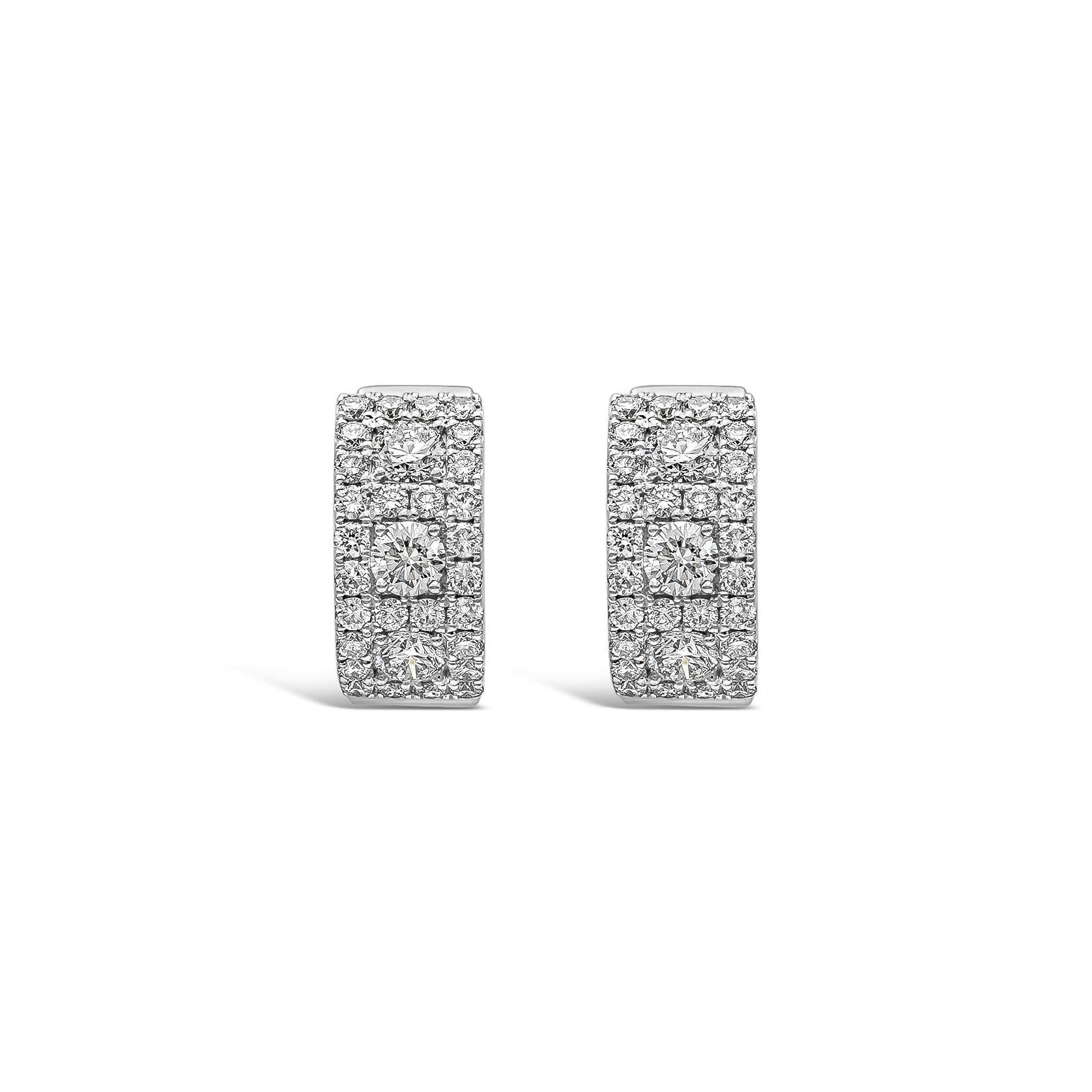 A stylish pair of huggie hoop earrings showcasing a row of round brilliant diamonds weighing 0.55 carats total, set in an 18k white gold setting. Accented with round melee diamonds weighing 0.60 carats total. Diamonds are approximately F color,