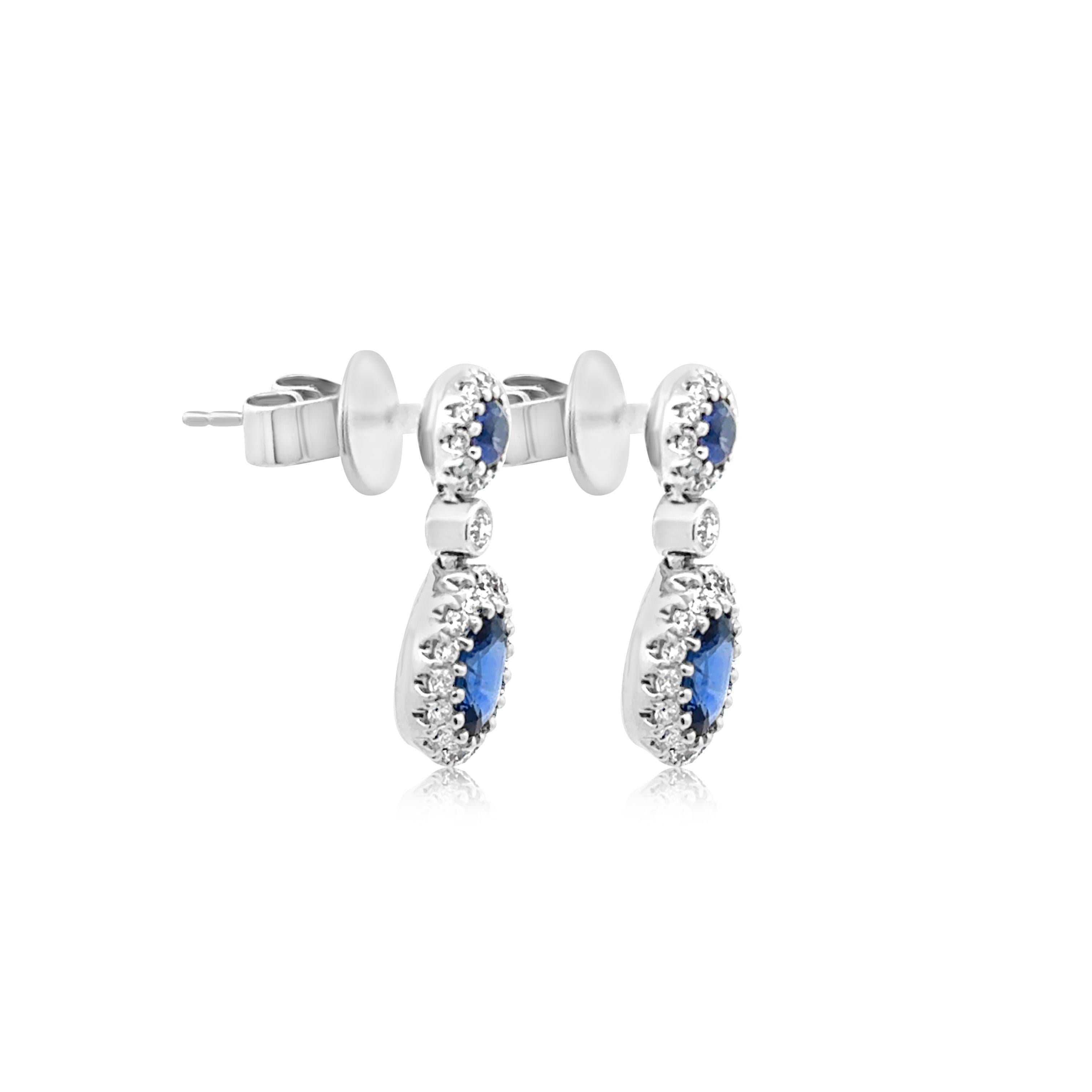 A stylish pair of drop stud earrings, featuring round and oval cut sapphires weighing 1.48 carats total, set on a multi-prong setting. Each sapphire is surrounded by a halo of round cut diamonds, set on a beautiful pavé design. Accented by a round