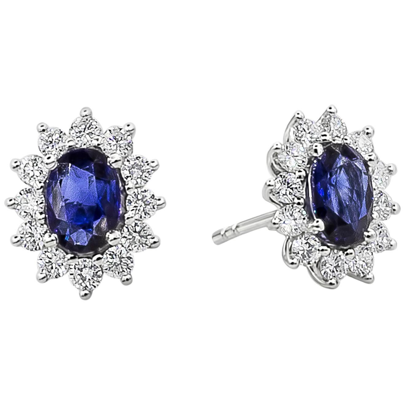 This beautiful color-rich gemstone earrings features an oval cut blue sapphires weighing 1.53 carats total. Elegantly surrounded by brilliant round diamonds set in a floral motif halo design, Diamonds weighs 0.79 carats total. Made in 18K White