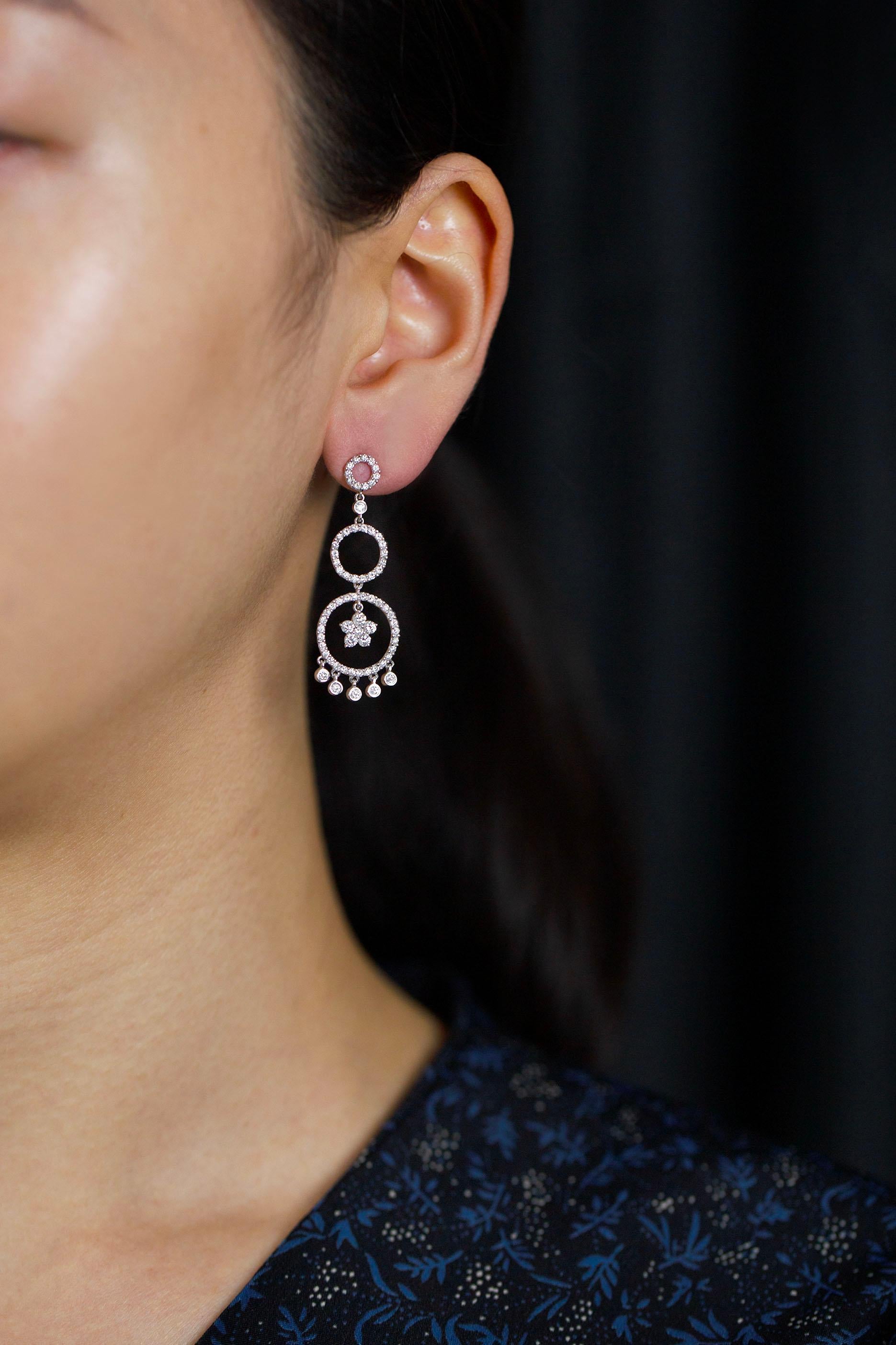 This stylish dangling earrings showcases three open-work, diamond encrusted circles that graduate in size as it drops down the earring mounted in a 18k white gold. On the last circle, the center designed to a floral motif and suspended below are 5