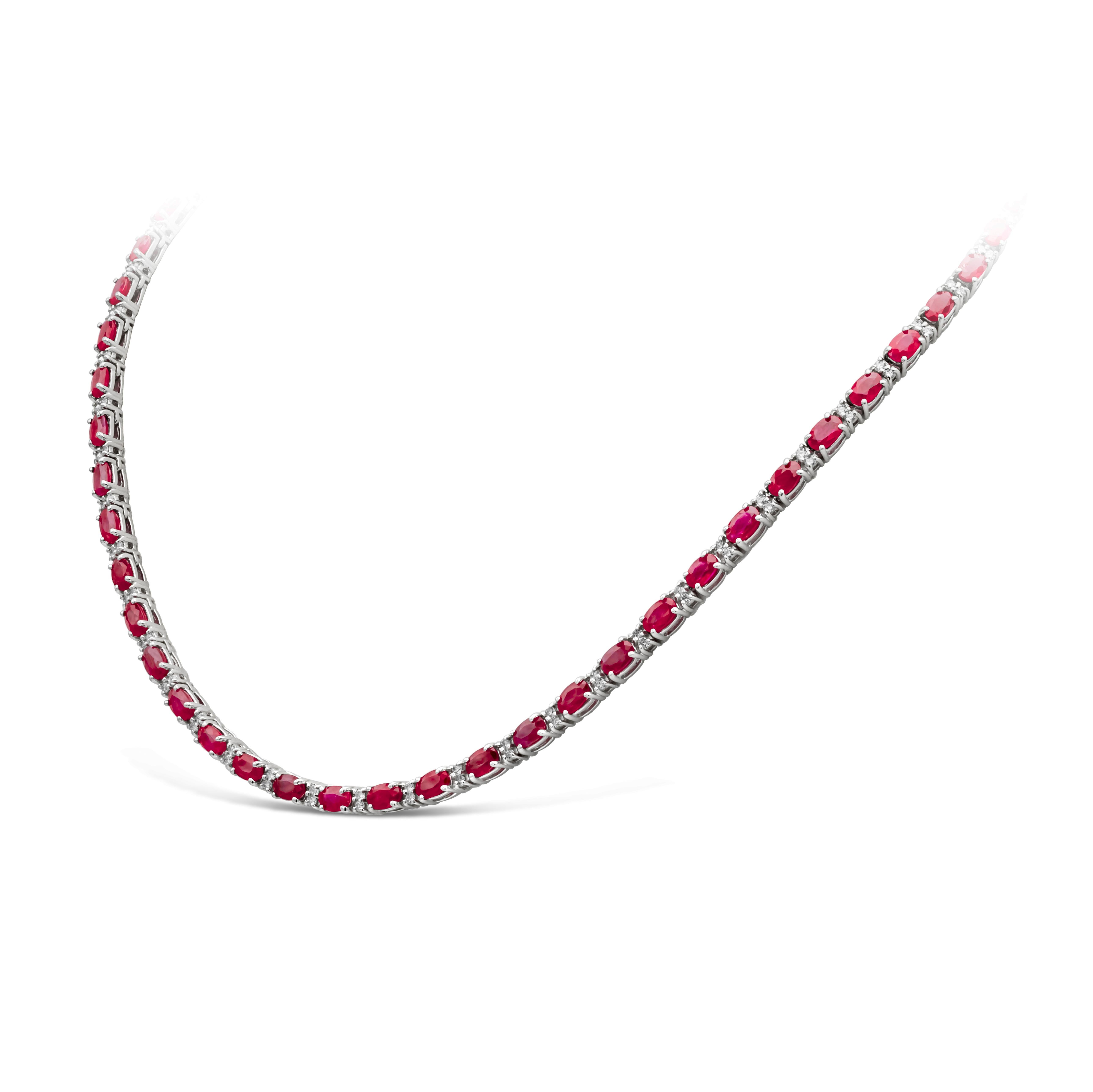 An incredibly color-rich tennis necklace showcasing 16.98 carats total oval cut red rubies, each elegantly spaced by two round brilliant diamonds weighing 1.49 carats total, F-G color and SI in clarity. Finely made in 14k white gold. Approximately