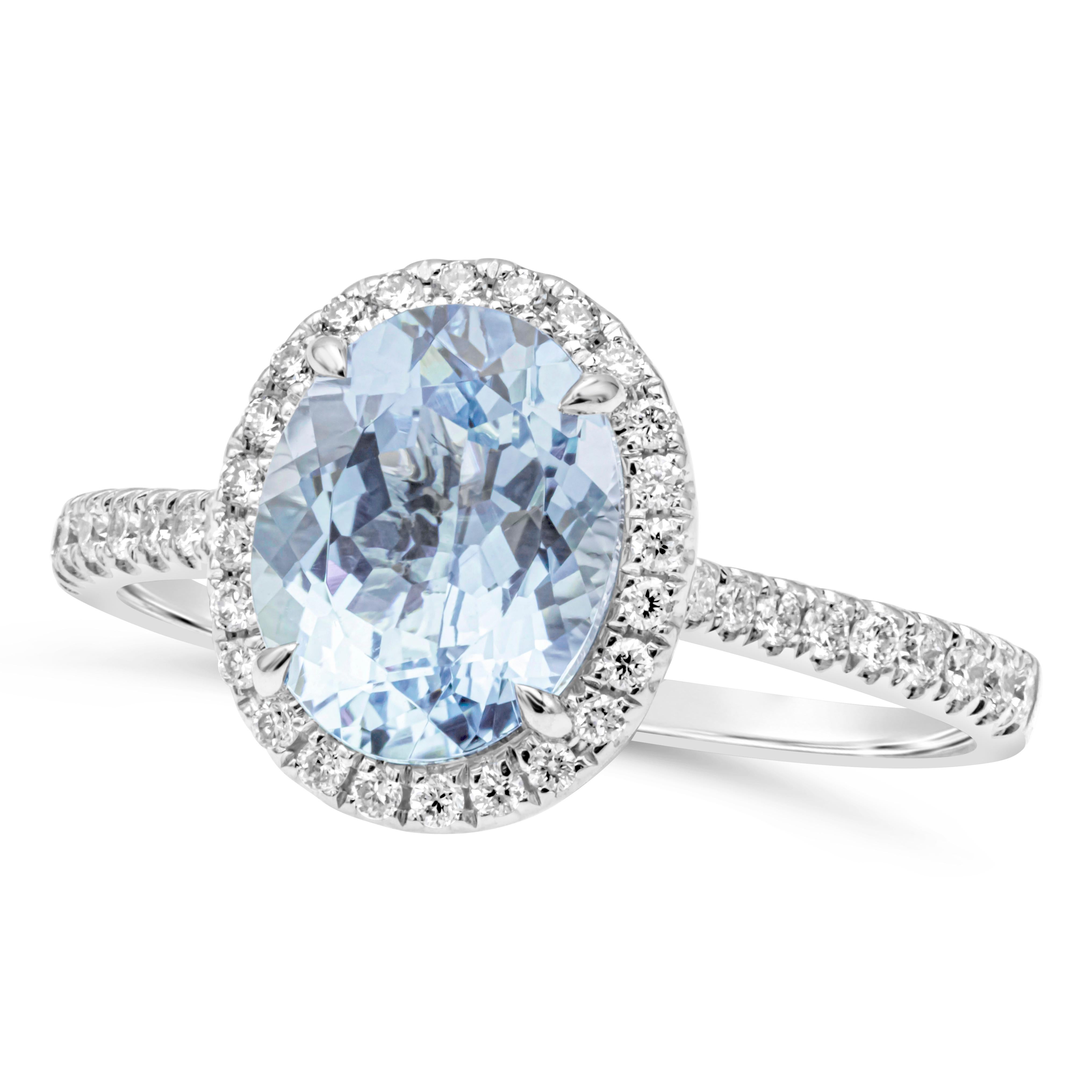 This versatile and beautiful halo engagement ring style showcasing an oval cut blue aquamarine weighing 1.69 carats total, set in a classic four prong setting. Elegantly surrounded by a row of brilliant round diamonds that continues on to the shank