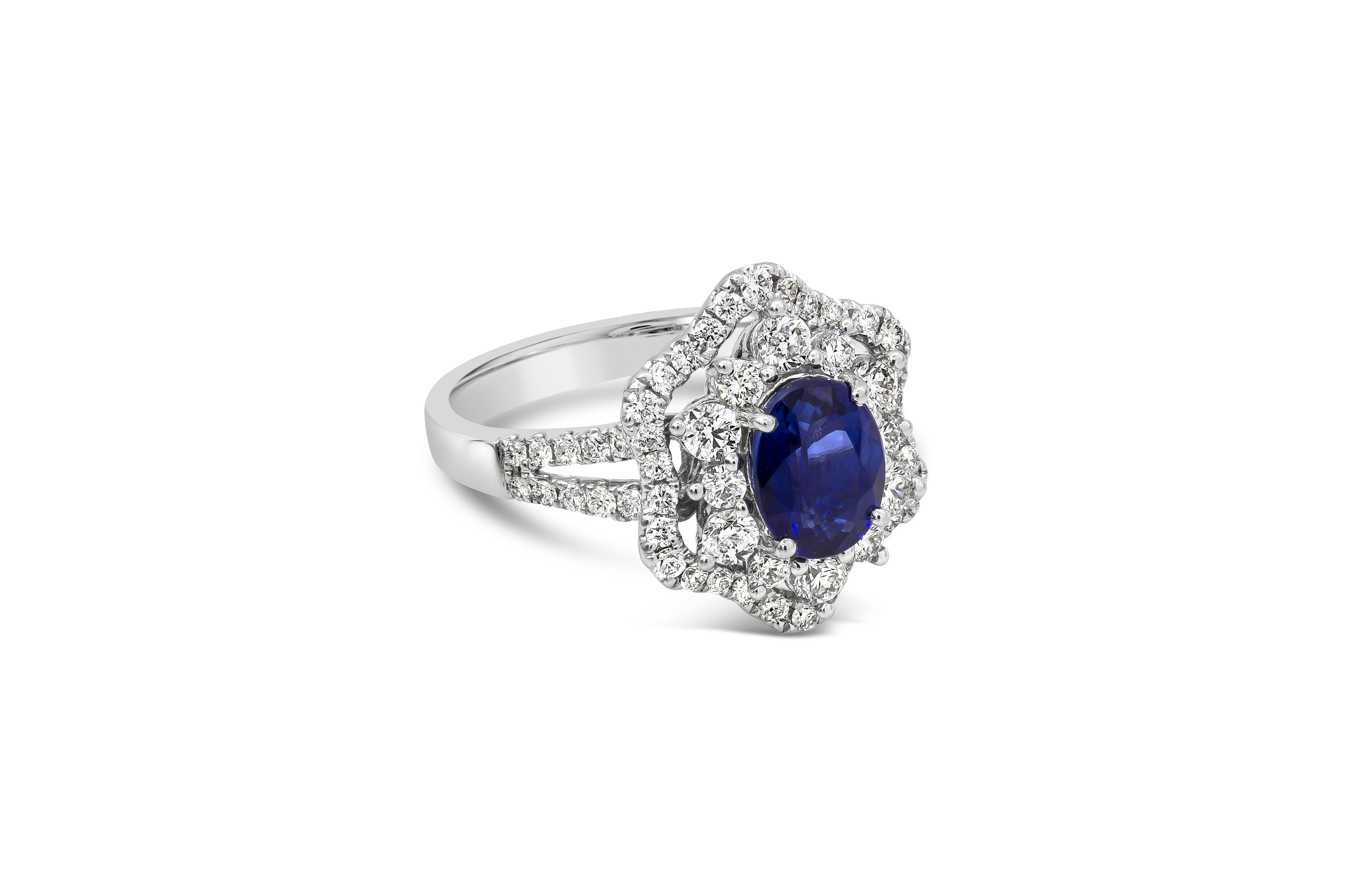 A unique flower halo engagement ring showcasing a 1.75 carat oval cut color-rich sapphire, surrounded by round brilliant diamonds in a open-work floral motif. Set in an 18k White Gold mounting accented by 62 brilliant round diamonds weighing 1.01