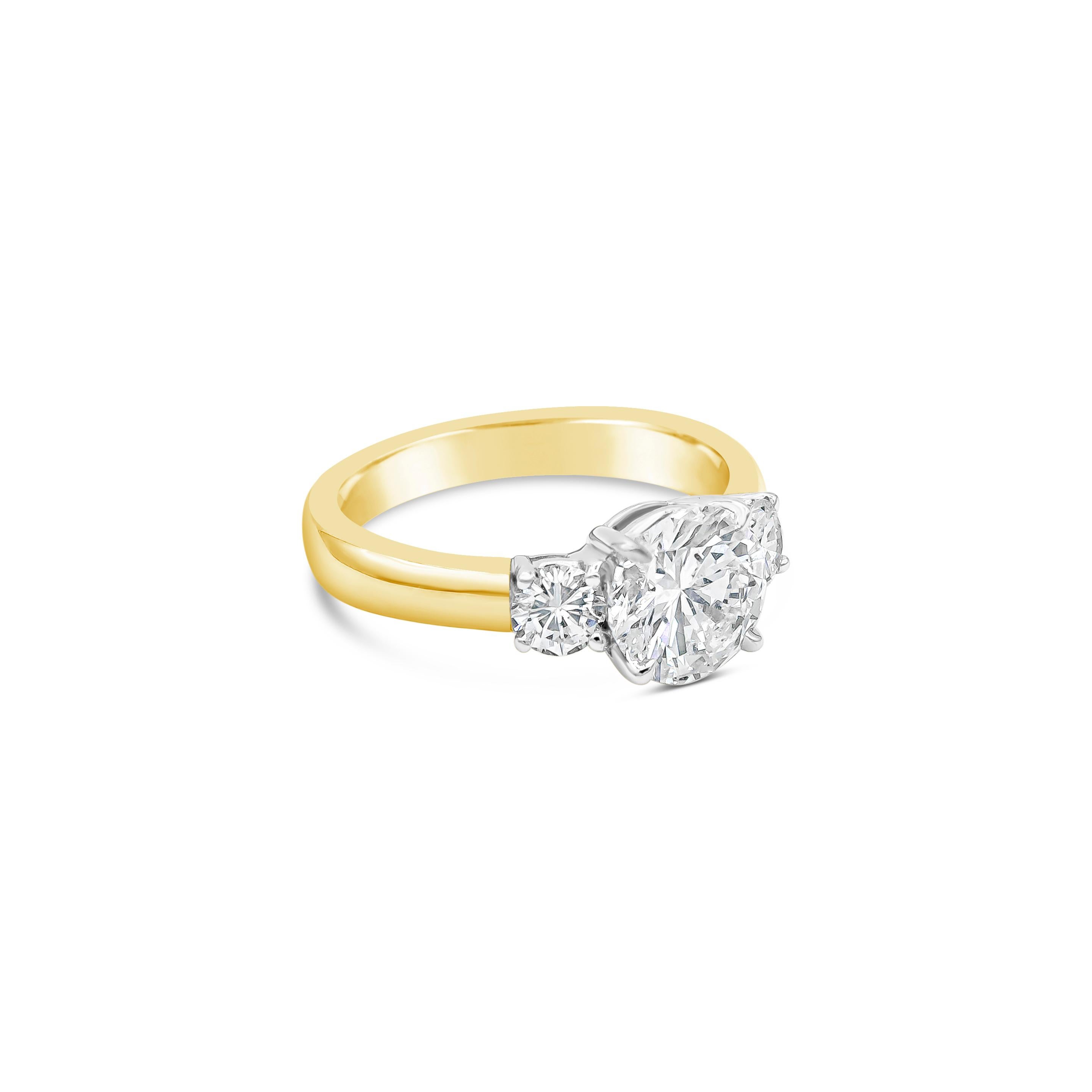 This ring showcases a round brilliant center stone that weighs at 1.50 carats, G Color and SI2 in Clarity. Flanked by a smaller brilliant round diamond on each side that weighs 0.40 carats total. Set in a 4 prong platinum crown attached to a comfort