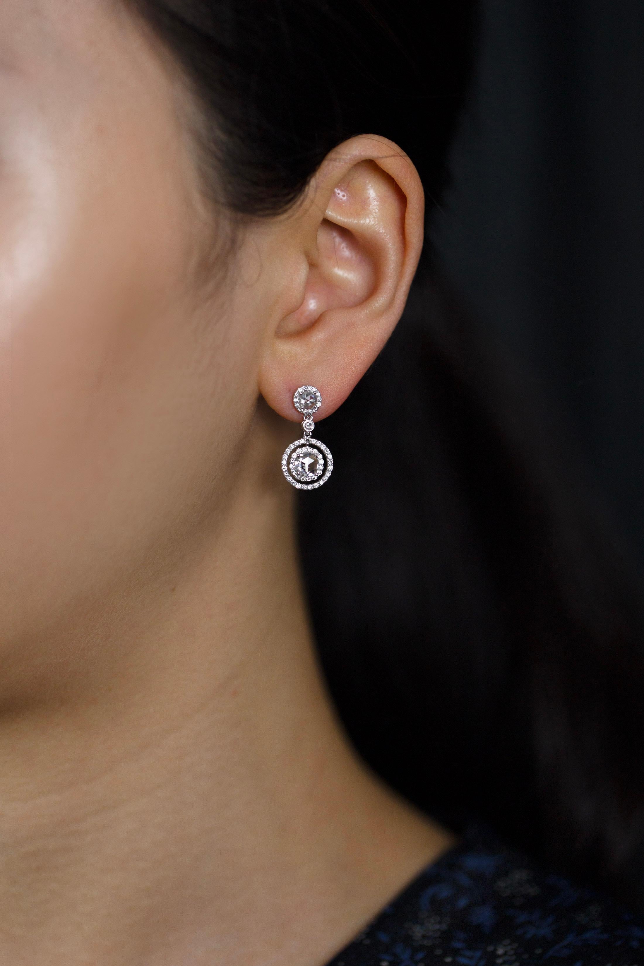 Exquise paire de boucles d'oreilles pendantes mettant en valeur des diamants taillés en rose et sertis dans un double halo ajouré incrusté de diamants ronds de taille brillant. Suspendue à un poteau également serti d'un diamant taillé en rose dans