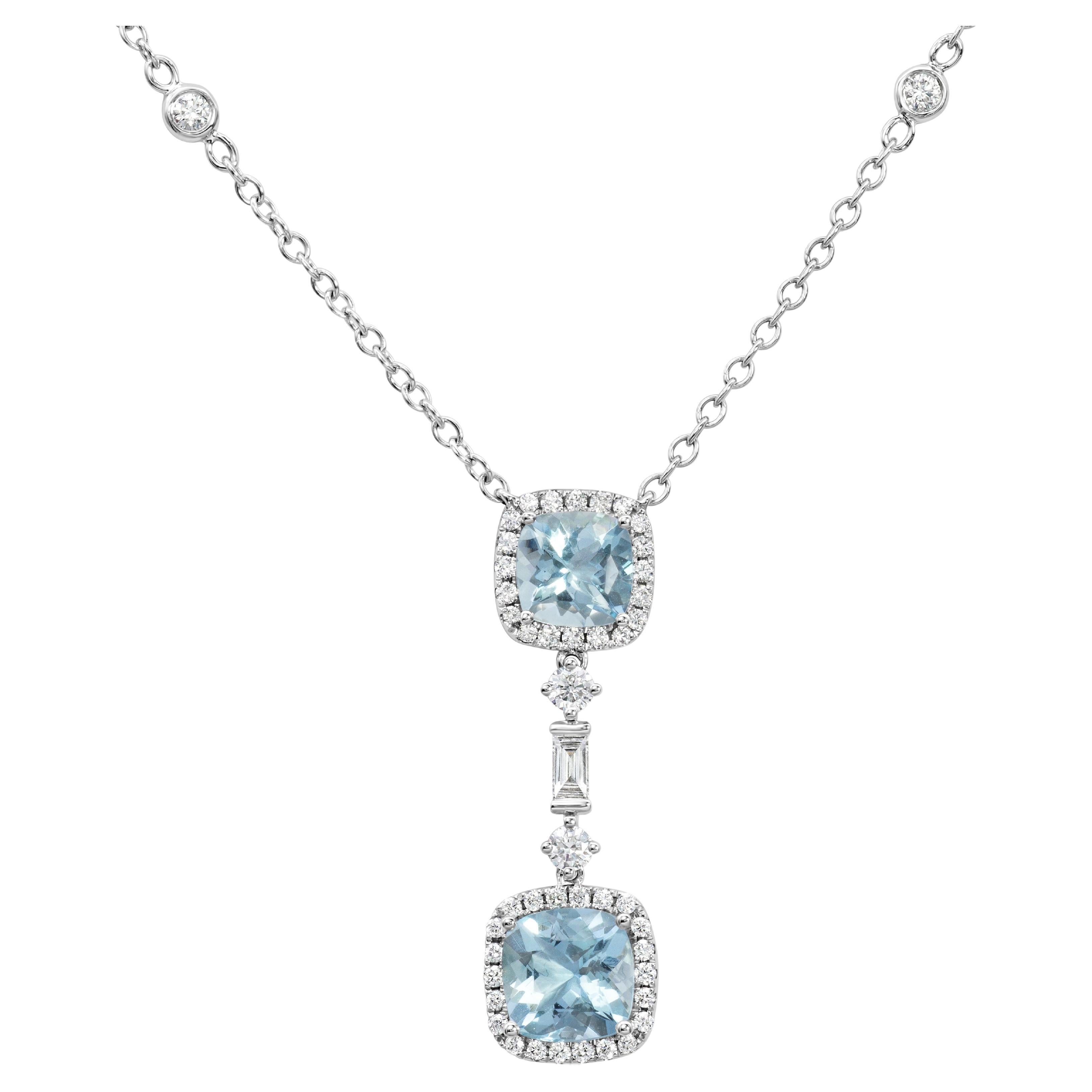 A stunning pendant necklace, showcasing two cushion cut aquamarines weighing 1.96 carats total, both surrounded by a halo of round cut diamonds. Accented by a line of two round and baguette cut diamonds, connecting the two aquamarines together.