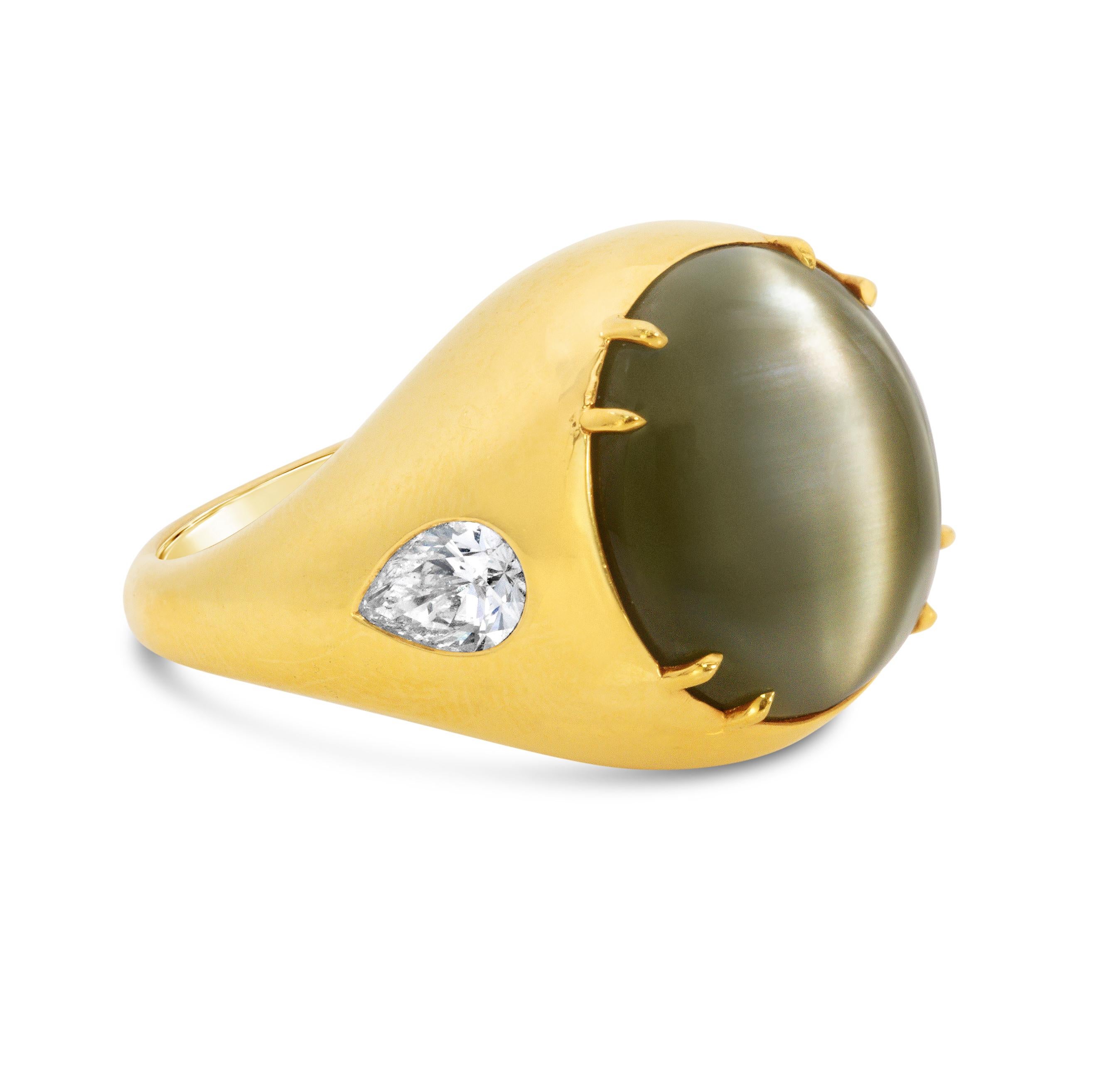 A stunning cocktail ring, featuring a very large cat's eye chrysoberyl oval cabochon weighing 28.30 carats, set in four double claw prongs. Accented by flushed pear shape diamonds weighing 1.03 carats total. Finely made with 18K yellow gold. Size