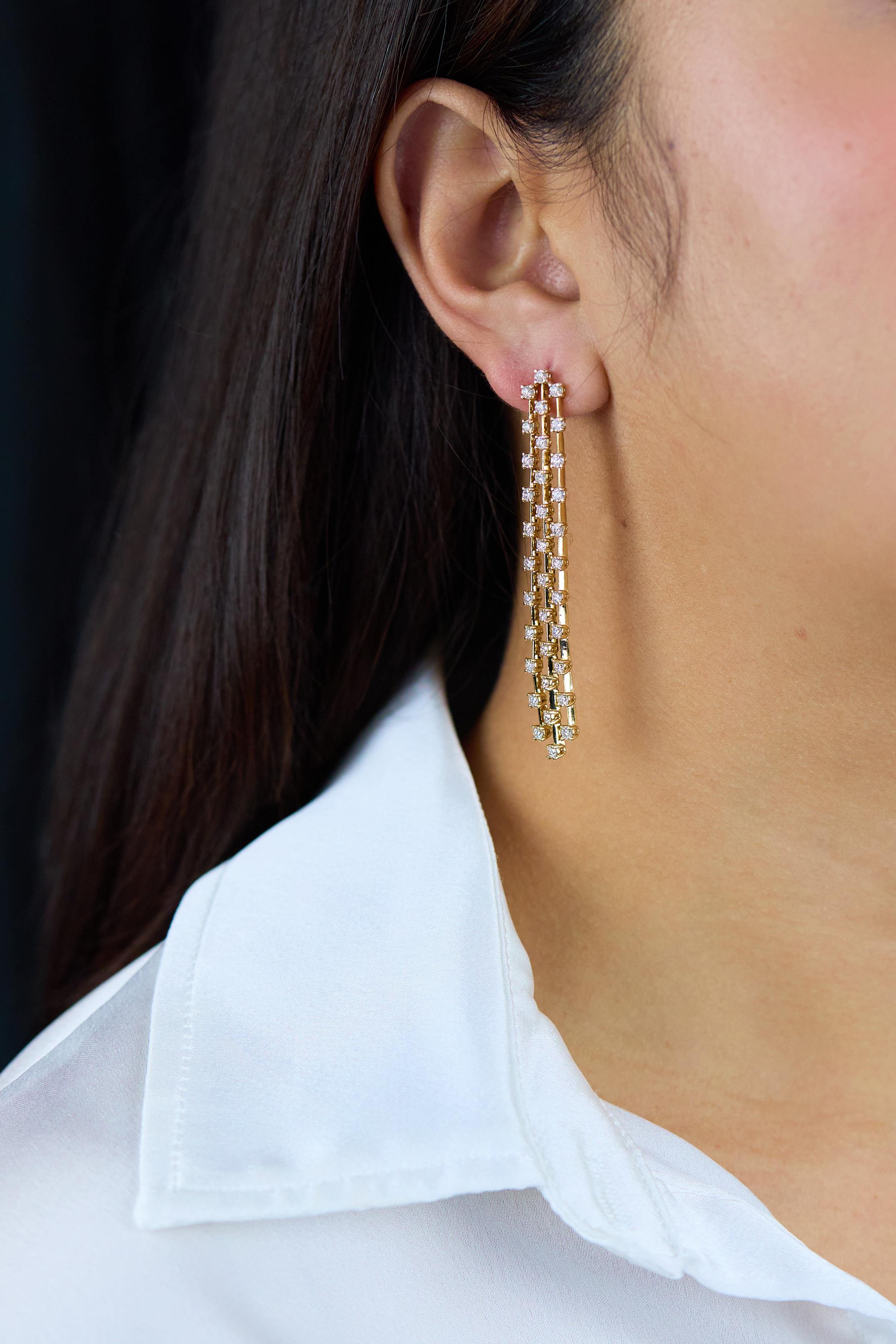 Une élégante paire de boucles d'oreilles chandelier, mettant en valeur trois rangées de diamants ronds de taille brillant, sertis dans un élégant design de chandelier en cascade. Finement réalisé avec une monture panier à quatre branches en or jaune