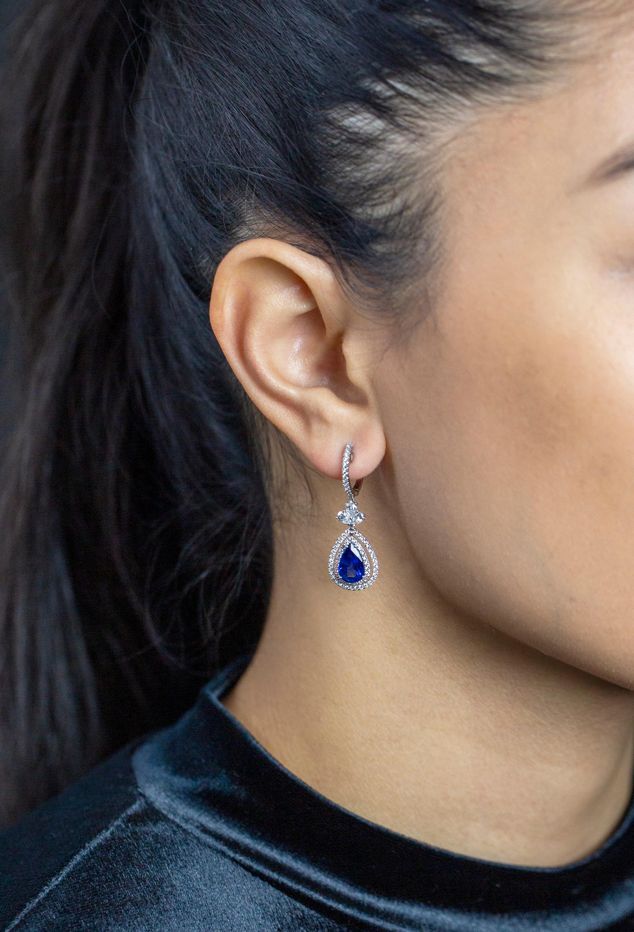 A stunning dangle earrings featuring pear shape blue sapphires weighing 4.18 carats total, surrounded by two rows of round brilliant diamonds in an free-dangling design. Suspended by an diamond encrusted hoop spaced by three pear shape diamonds.