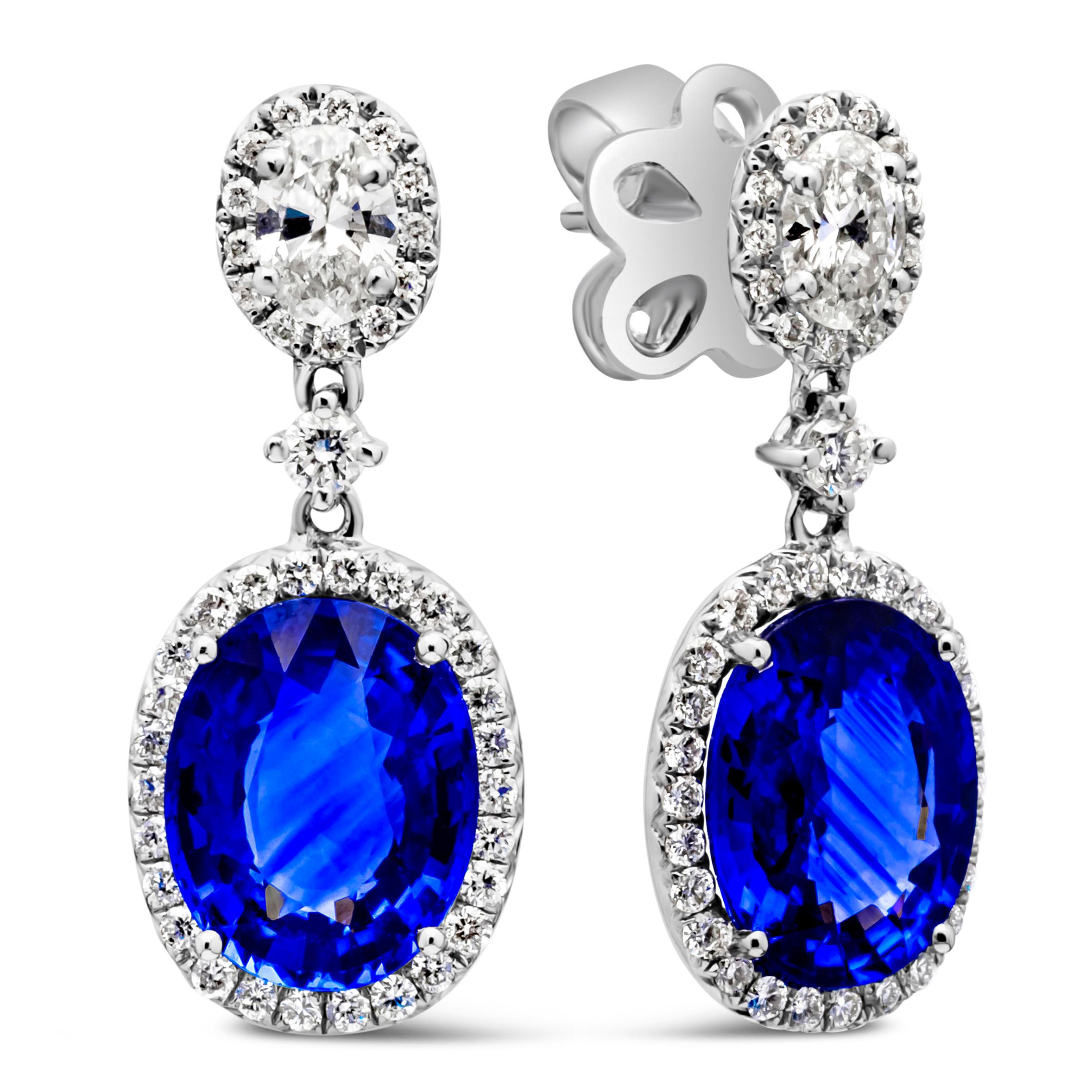 A beautiful and vibrant pair of dangle earrings, showcasing color-rich blue sapphires weighing 4.38 carats total, elegantly set with a halo of round brilliant cut diamonds. Suspended on oval cut diamonds also set with a diamond halo and spaced with