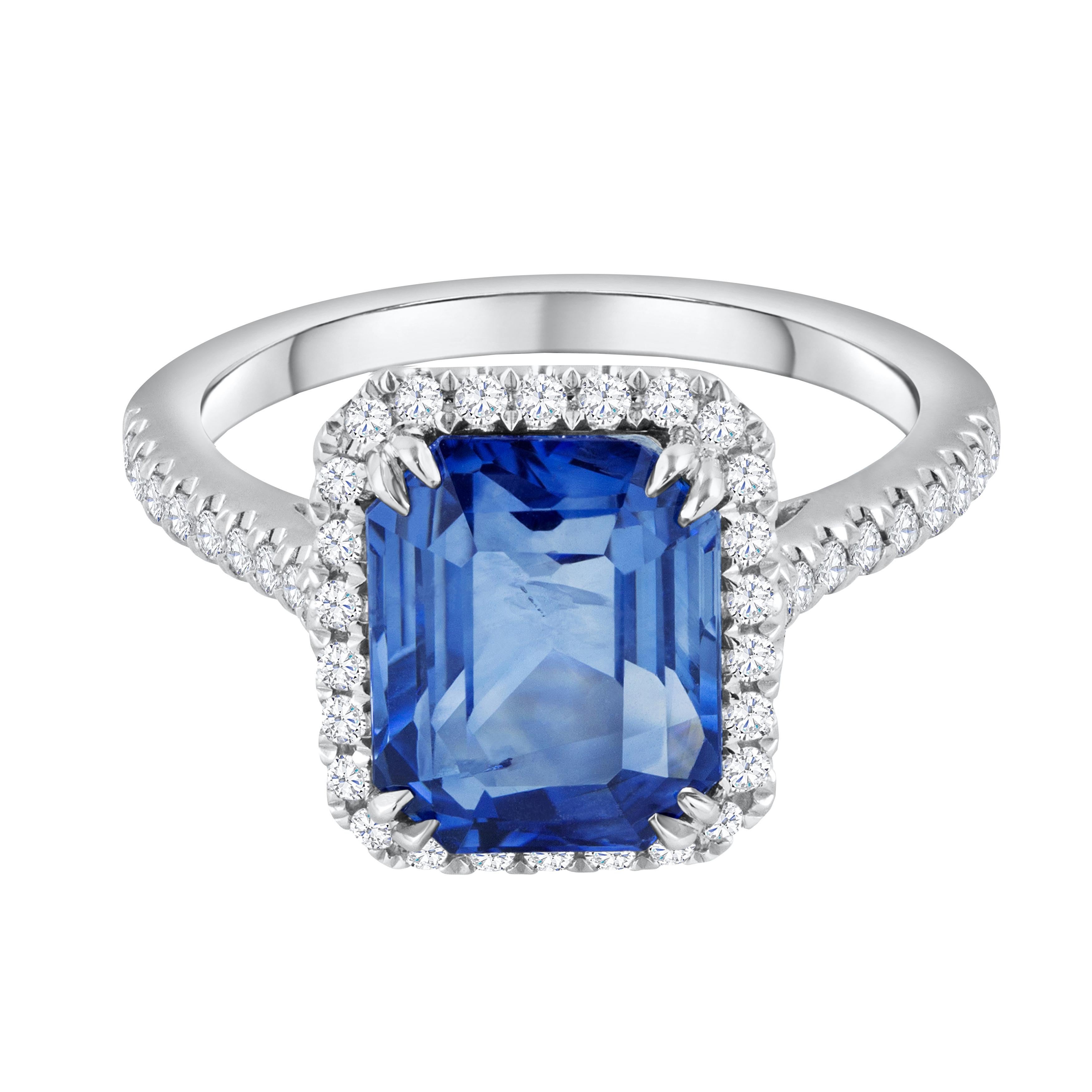 A gorgeous engagement ring, featuring a 4.88 carats emerald cut blue sapphire, set on an eight prong setting. Surrounded by a halo of round cut diamonds and accented by a diamond encrusted shank with a half-eternity design. Accent diamonds weigh