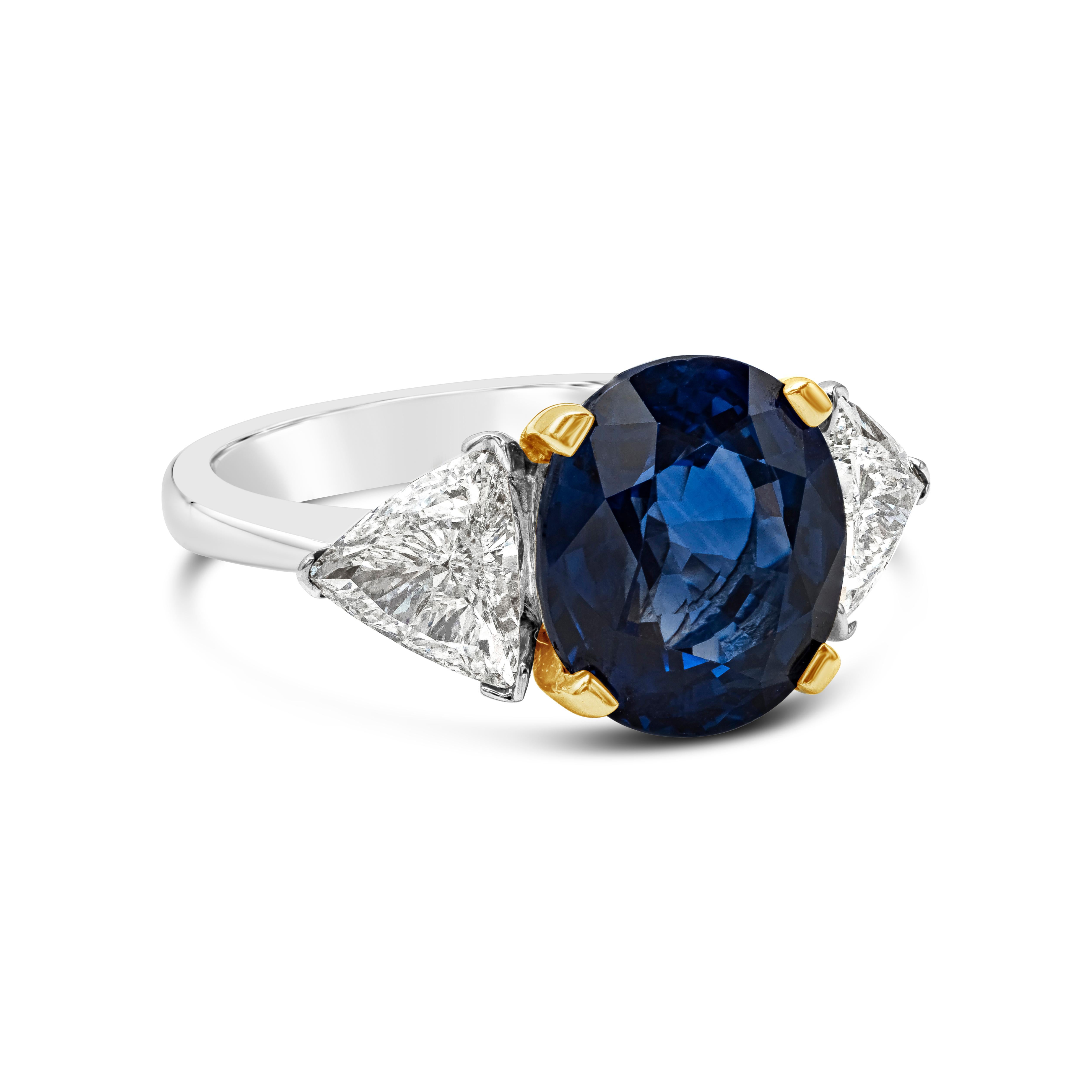 This color-rich and brilliant three-stone engagement ring features a color-rich 5.28 carats oval cut blue sapphire originated from Sri Lanka. Set in a classic four prong 18k yellow gold basket setting. Flanked by two trillion diamonds on either side