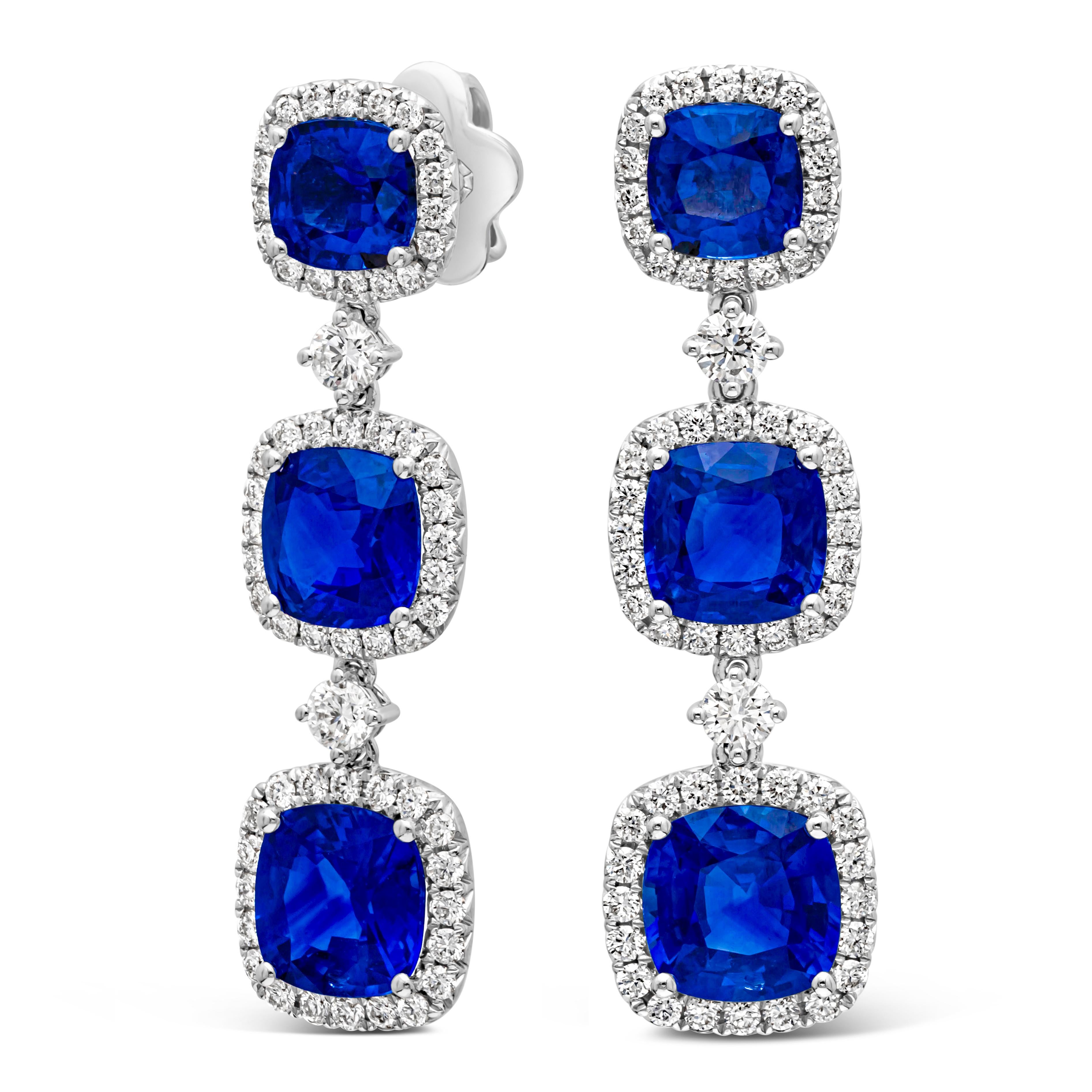 This stunning each dangle drop earring showcases three cushion cut color-rich blue sapphires surrounded by brilliant round cut diamonds in a halo design. Elegantly set in a dangle style and spaced with brilliant round diamonds. Blue sapphires weigh