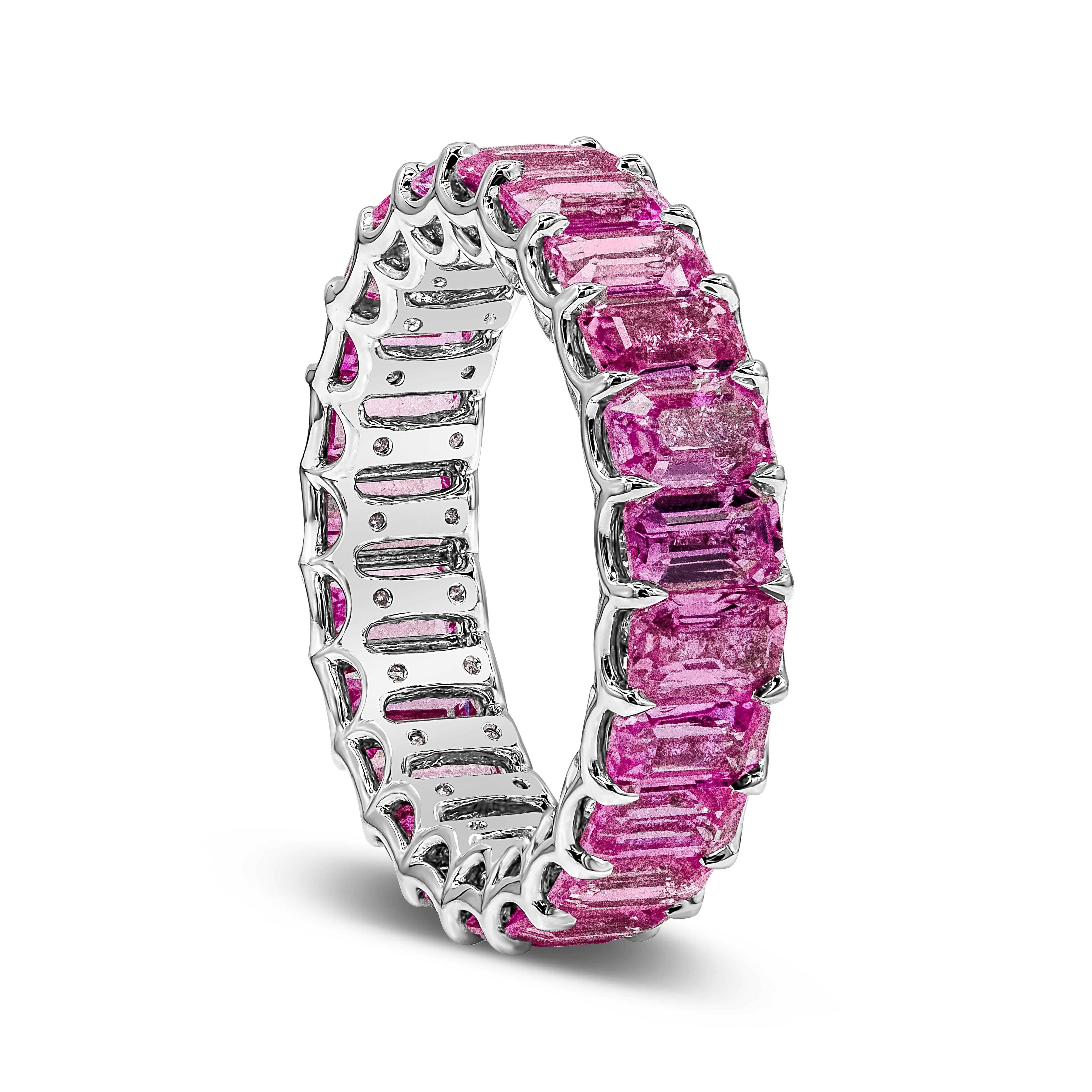 A unique eternity ring style showcasing a row of emerald cut pink sapphires weighing 7.66 carats total. Inside the basket of the sapphires are round brilliant diamonds set underneath the gemstones to make the piece sparkle. Melee brilliant round