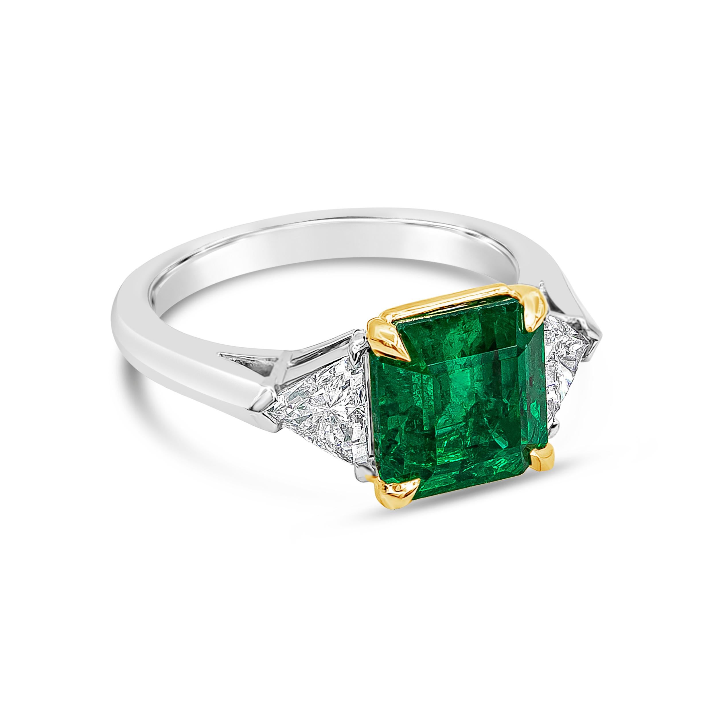 A timeless engagement ring style showcasing a 3.16 carats emerald cut green emerald, set in a 18K Yellow Gold four prong basket setting. Flanked by brilliant trillion diamonds on each side weighing 0.70 carats total. Made in Platinum band and Size