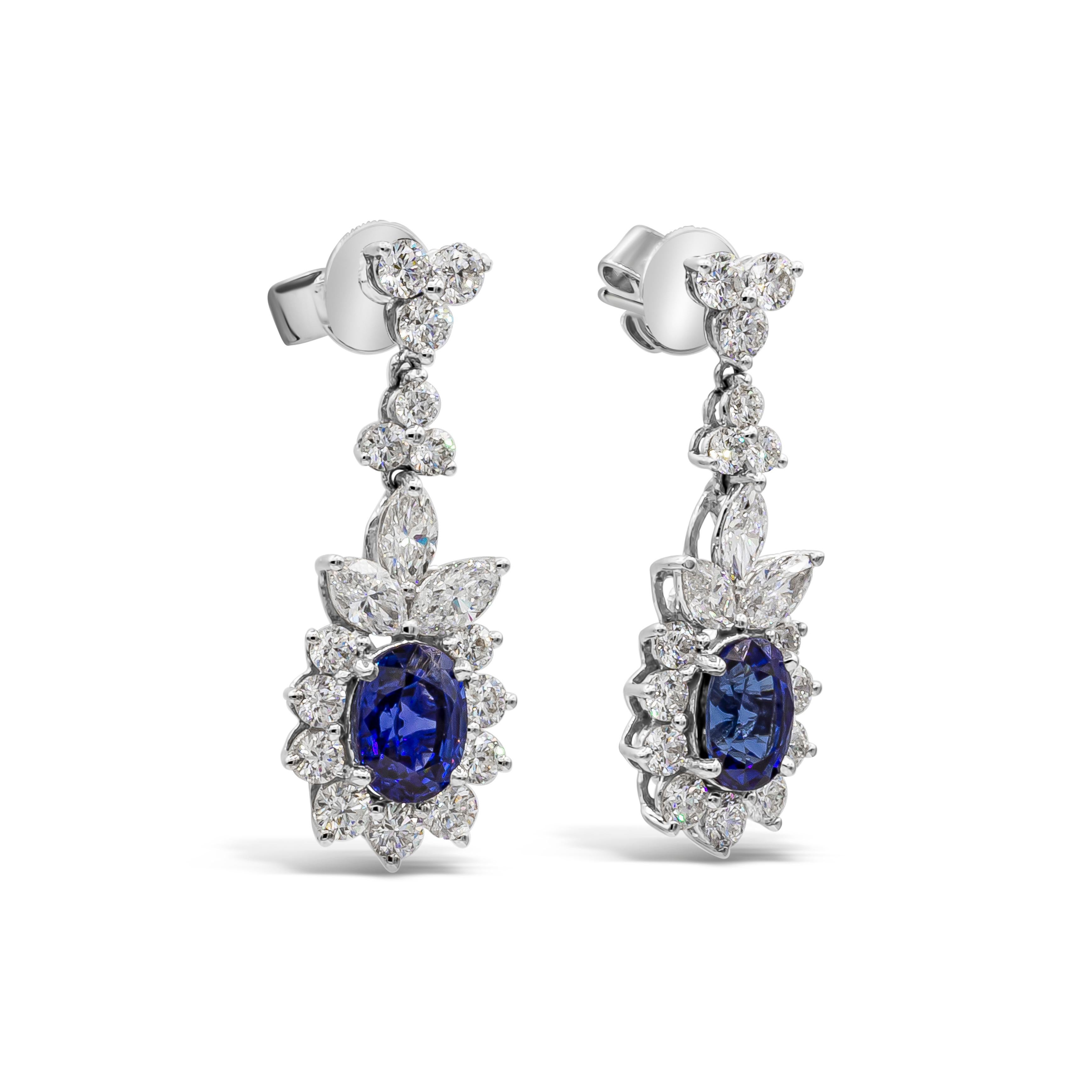These elegant and classic dangle earrings showcasing beautiful oval cut blue sapphires weighing 3.72 carats total. Accented by a row of round brilliant diamonds in a halo design, suspended and spaced by marquis cut diamonds and attached to a 3 stone