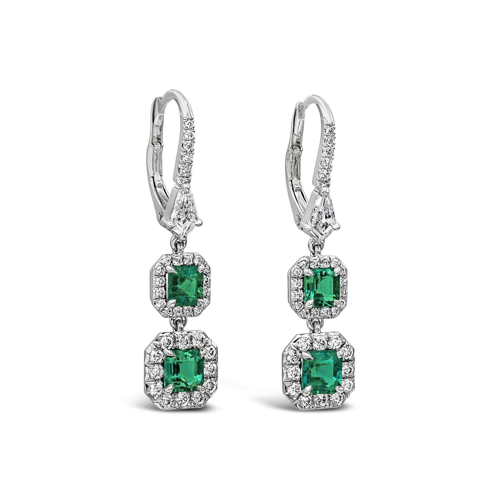 A spectacular piece of jewelry showcasing 2 dangling vibrant Colombian emeralds on each earring surrounded by a brilliant round diamond halo, connected to a diamond encrusted platinum lever-back. Emeralds weigh 1.53 carats total, diamonds weigh 0.94