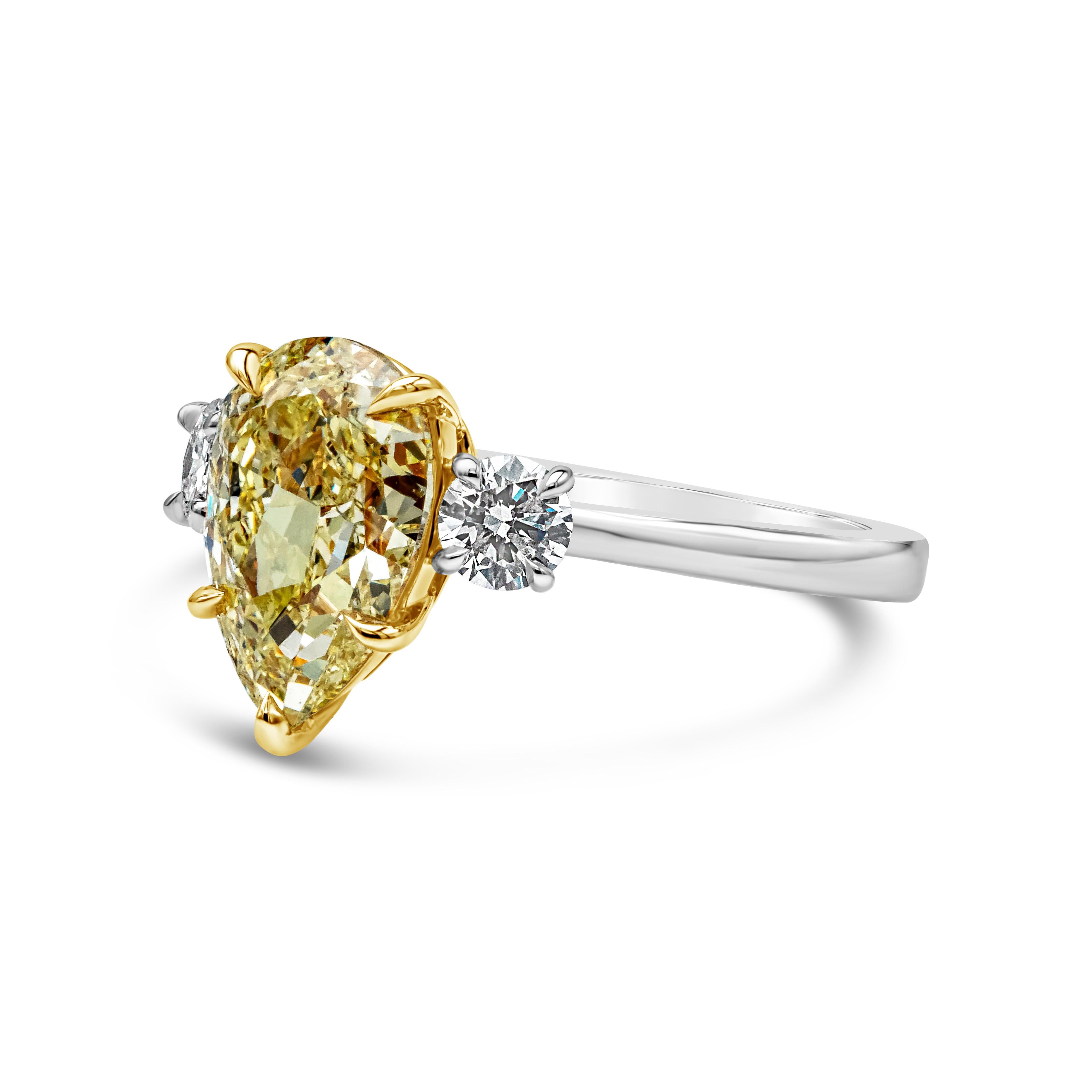 This beautiful three stone engagement ring style showcasing a GIA Certified pear shape fancy yellow diamond, SI2 in Clarity, set in a five prong basket setting. Flanked by brilliant round diamonds on each side weighing 0.38 carats total, F Color and
