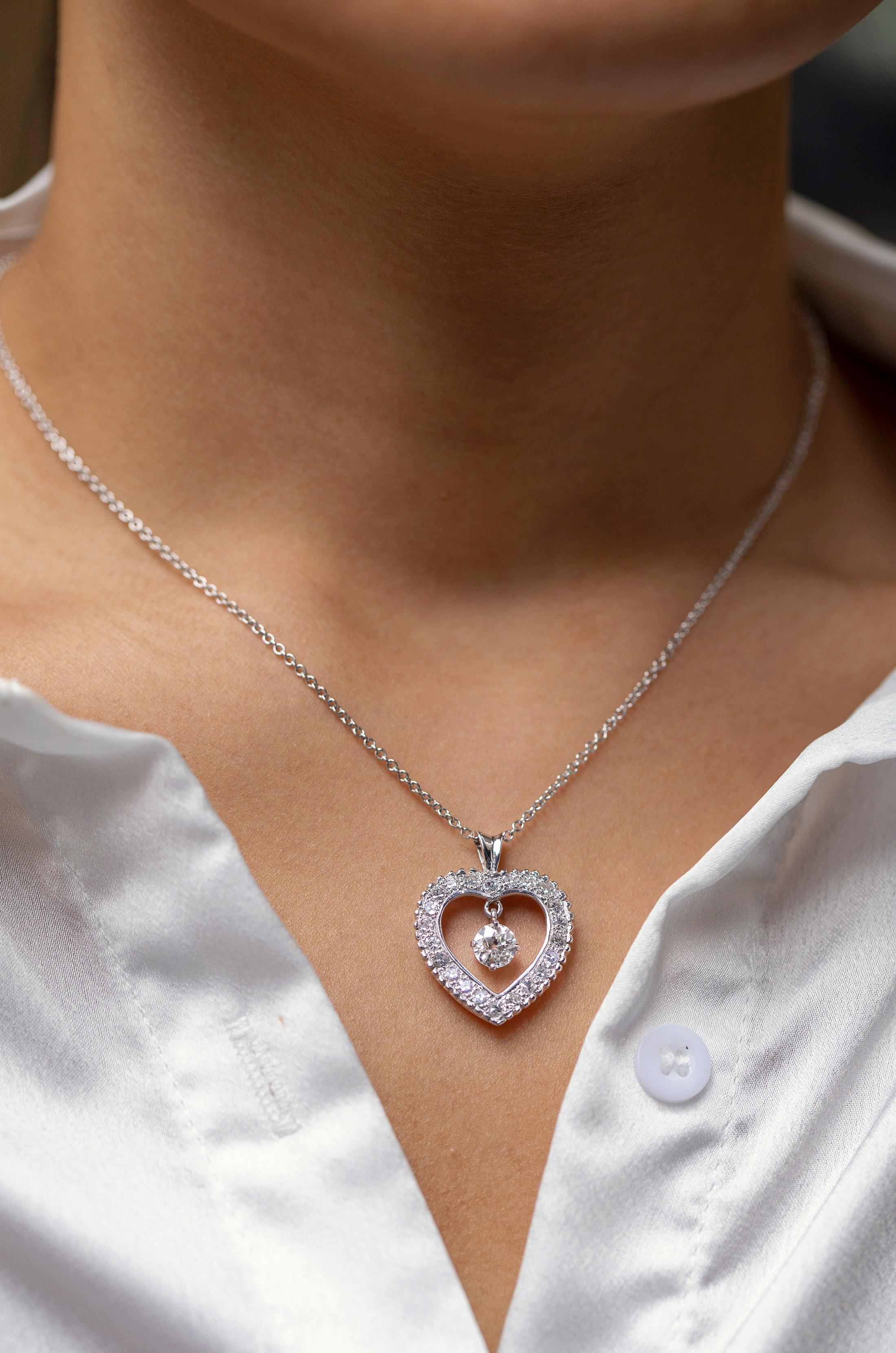 A pretty pendant necklace, showcasing a 0.72 carat old European cut diamond, set in a dangling open-work design. Surrounded by French cut round diamonds weighing 1.09 carats total, set on a heart shape mounting. Finely made with 18K white