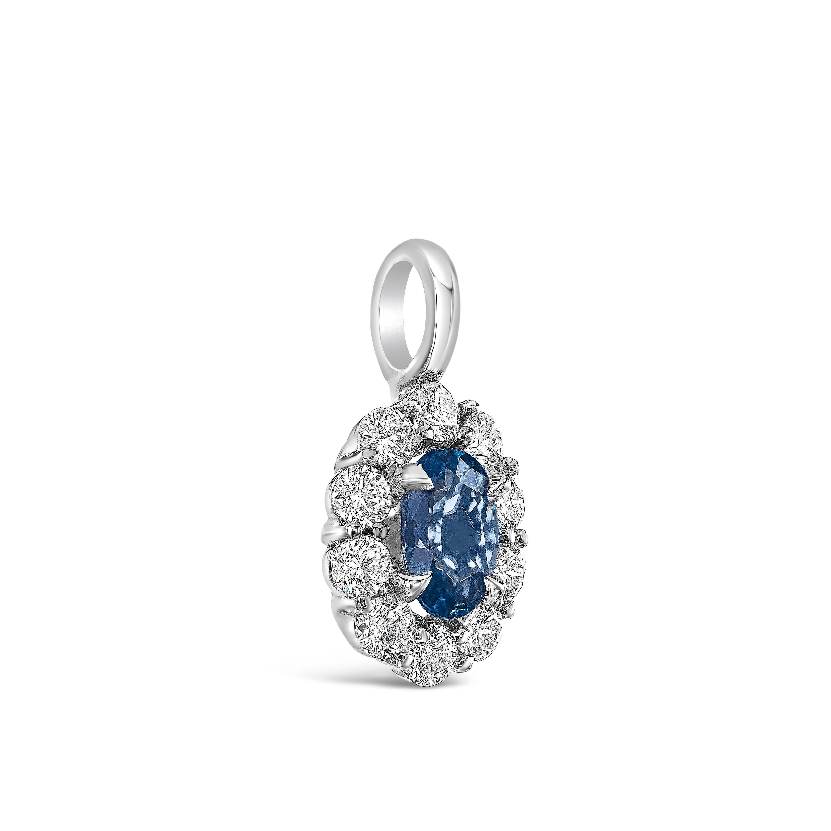 A classic and versatile pendant necklace showcasing a 0.38 carat oval cut blue sapphire, surrounded by a single row of round brilliant diamonds weighing 0.35 carats total. Set in 18K white gold. Suspended on an 18 inch white gold chain. 

Roman