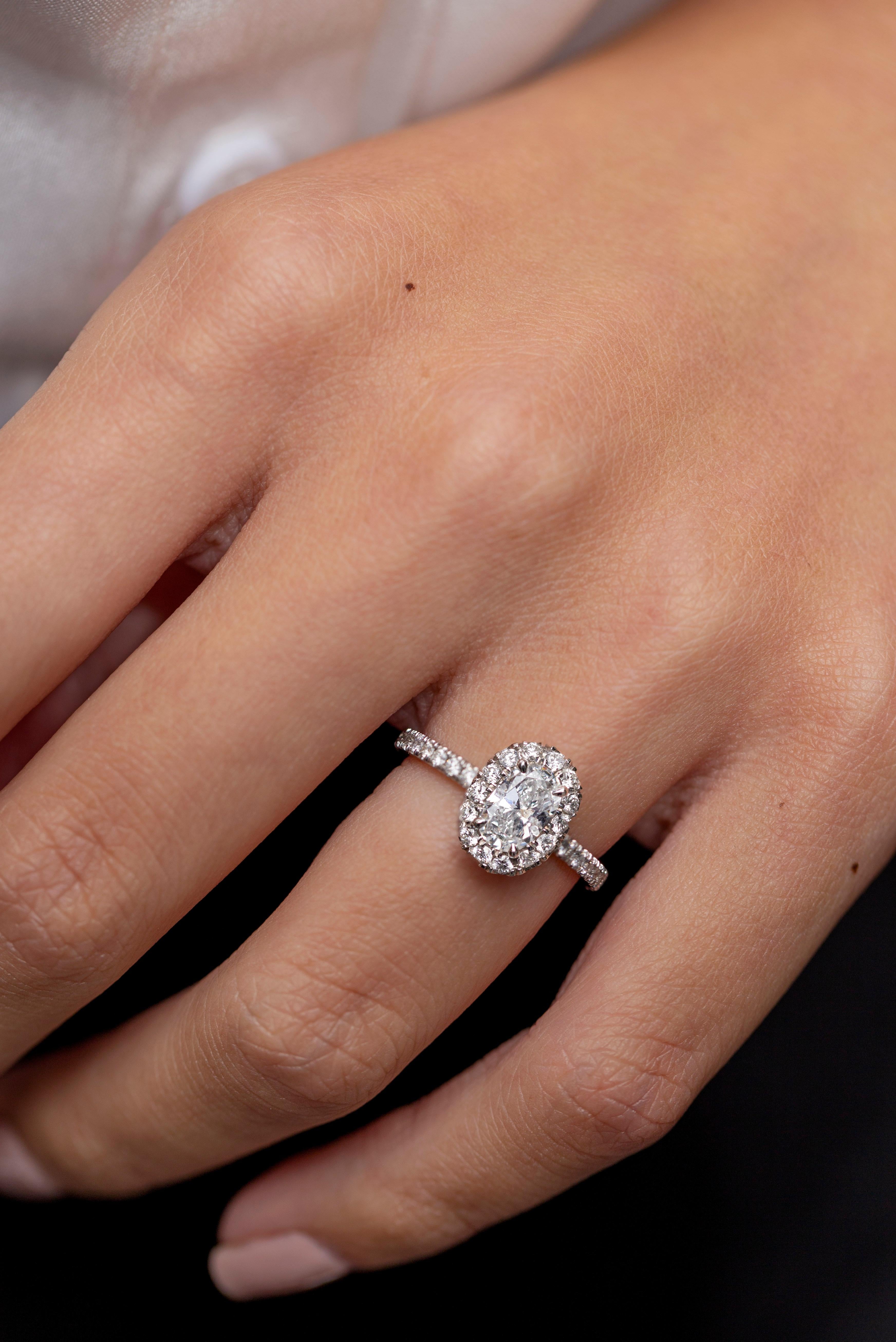 Ein gut gearbeiteter Verlobungsring mit einem oval geschliffenen Diamanten von 0,60 Karat in einer nahtlosen Diamant-Halo-Fassung. Fein gearbeitet in einer polierten Platinkomposition, die mit runden Diamanten in halber Ewigkeitsfassung akzentuiert