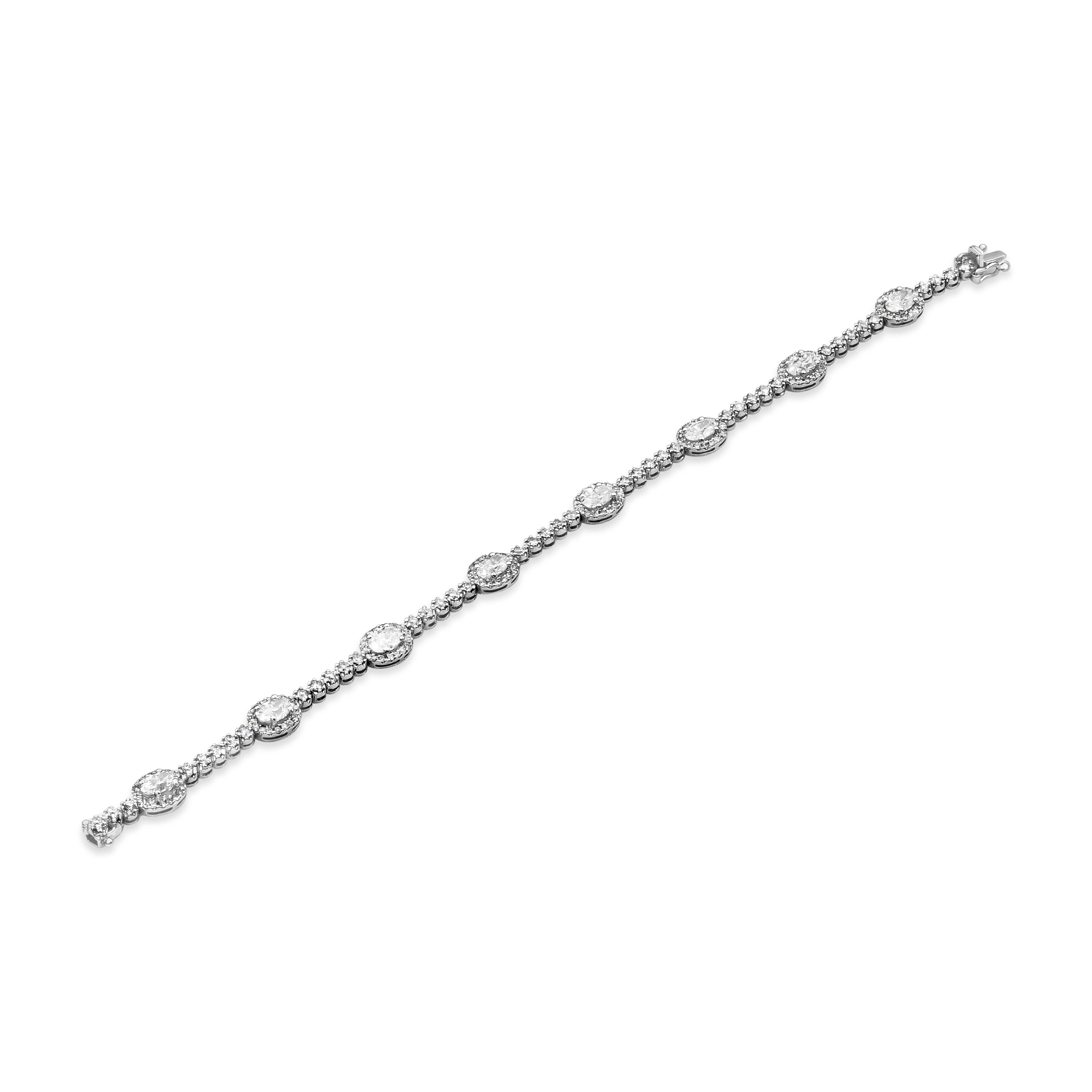 A classic diamond halo style tennis bracelet showcasing 2.46 carat total oval cut diamonds surrounded by a row of brilliant round diamonds, separated by five round diamonds. Weight of the accenting round diamonds is 1.52 carats total. Made with 18K