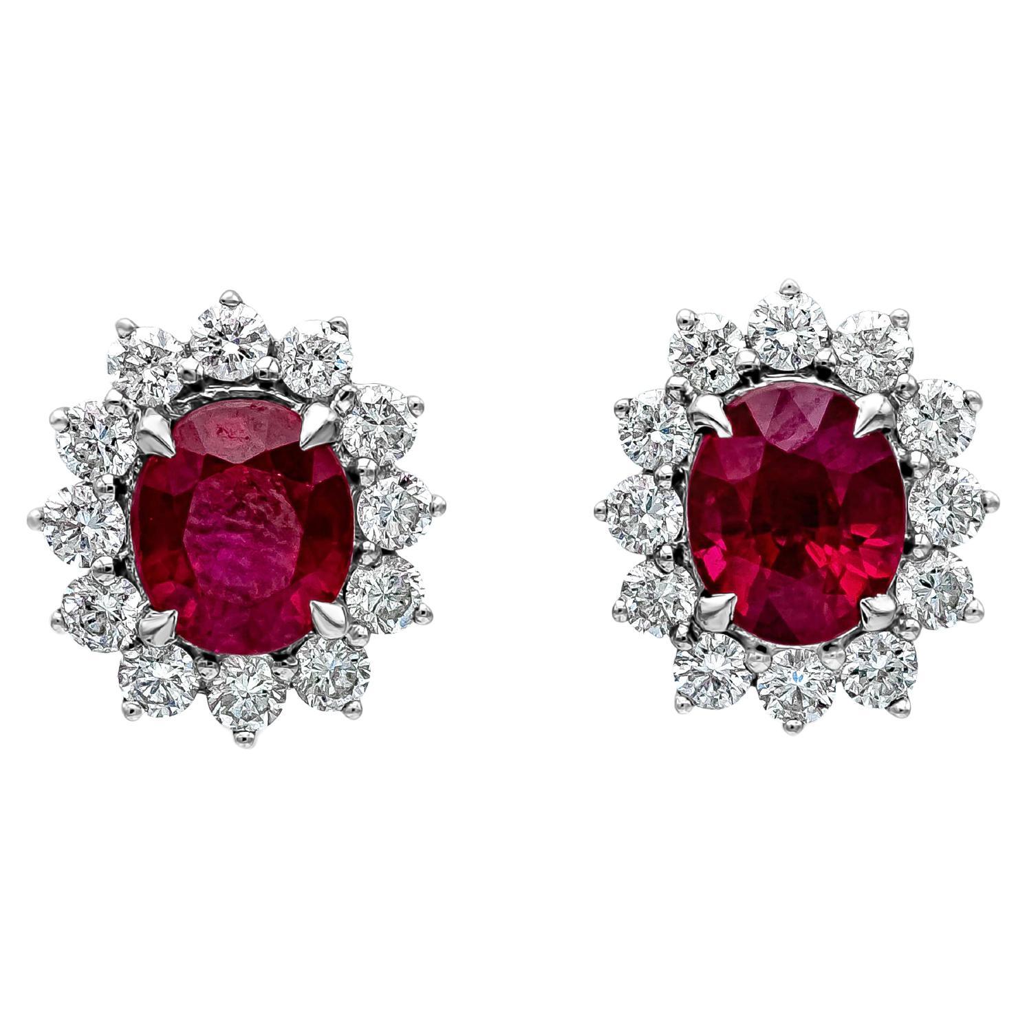 A classic pair of stud earrings showcasing vibrant red oval cut rubies, surrounded by a single row of round brilliant diamonds in a floral motif design. Rubies weigh 2.09 carats total, diamonds weigh 0.59 carats total. Made in 18K White Gold.

Roman