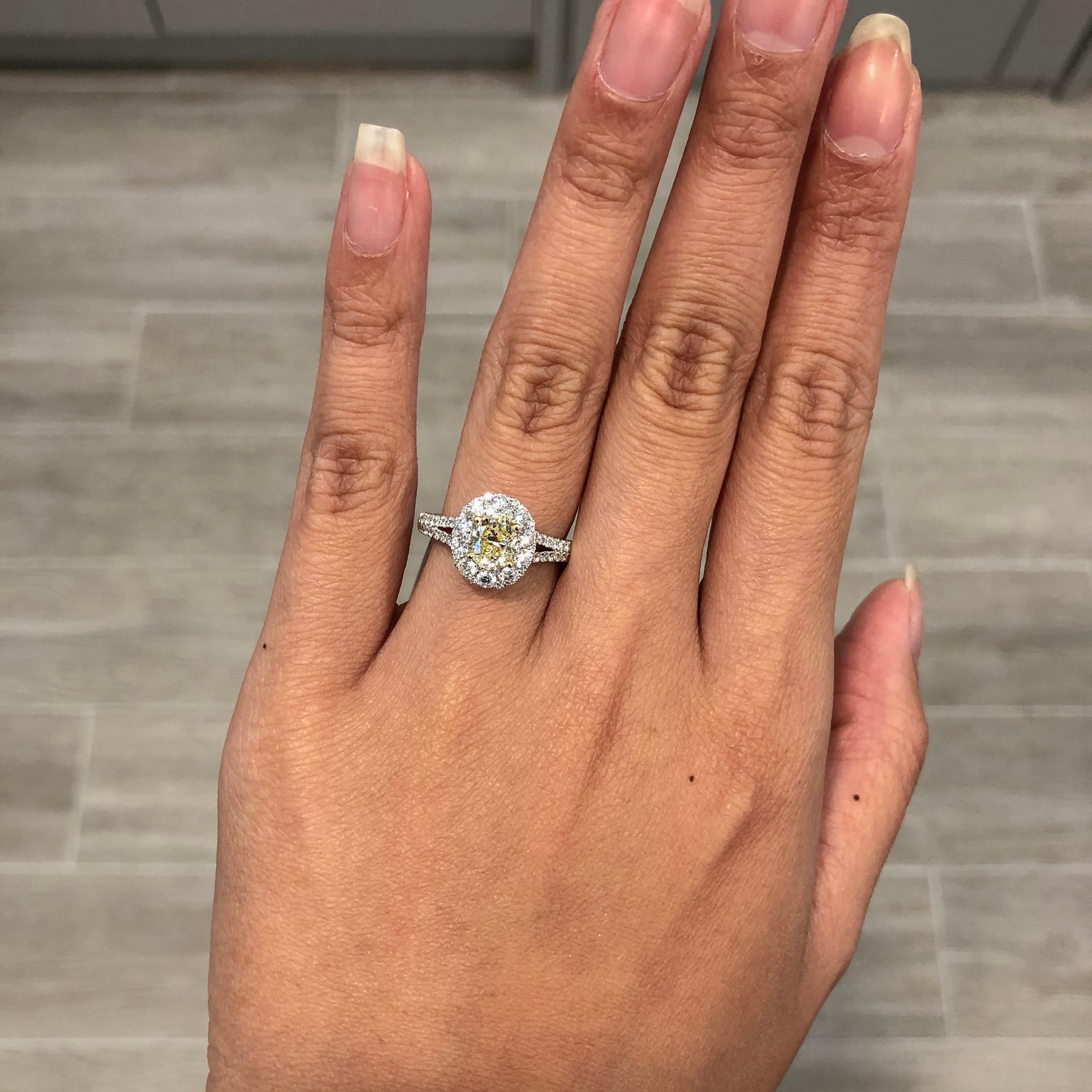 Showcasing an oval cut light yellow diamond center stone weighing 0.97 carats, surrounded by round brilliant diamonds. Set in a split-shank setting accented with round brilliant diamonds. Diamonds weigh 0.89 carats total. Made in 18 karat white