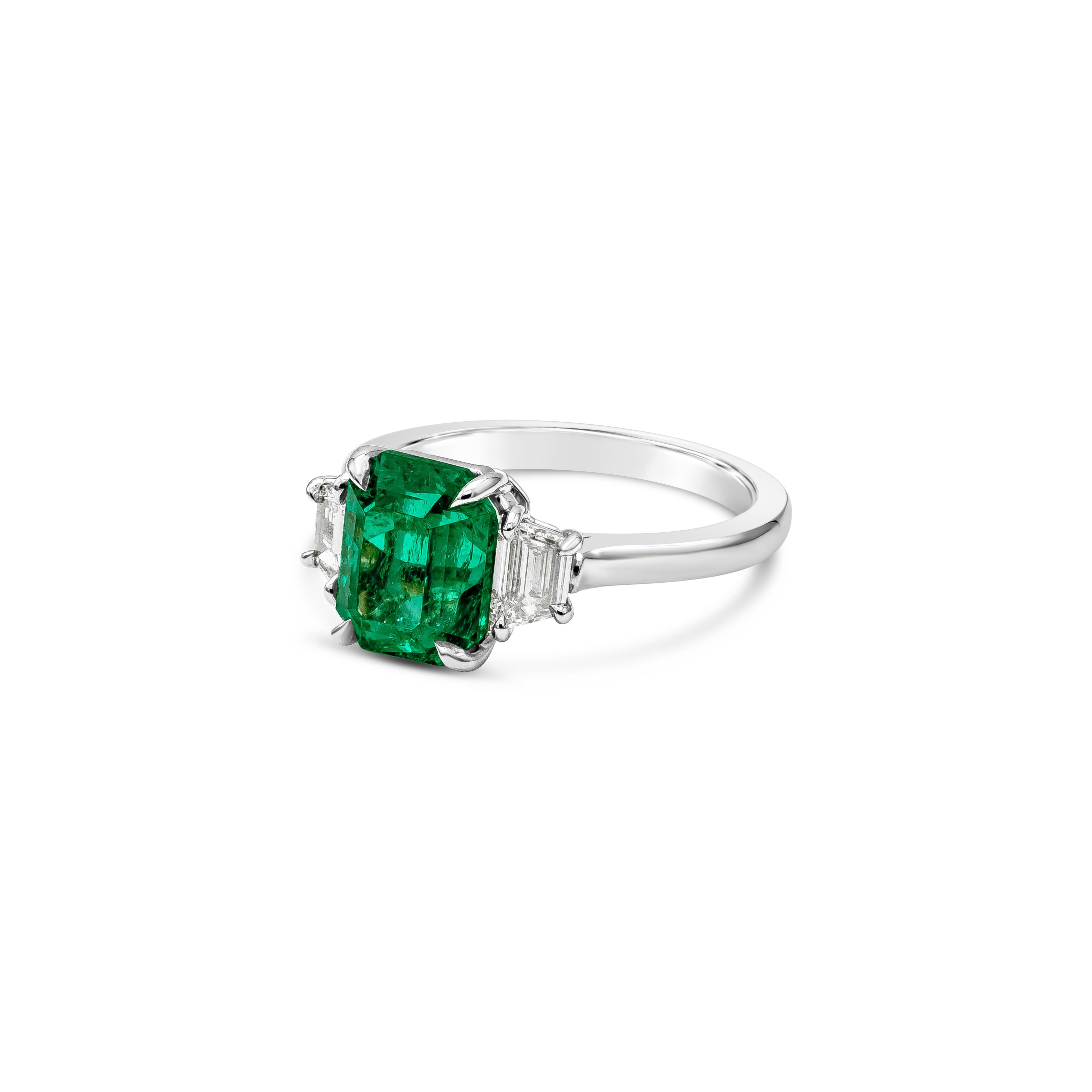 This stunning and elegant engagement ring showcasing a AGL certified color-rich radiant cut green emerald center stone weighing 2.49 carats, G color VS in clarity and set in a classic four prong basket setting. Flanked by two brilliant trapezoid