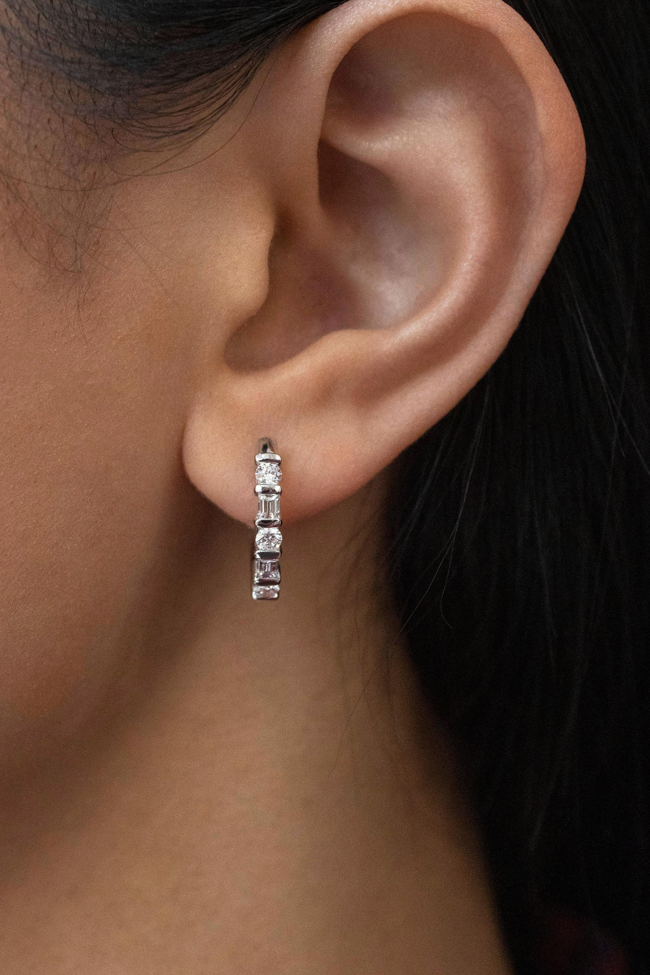 A simple pair of huggie hoop earrings showcasing alternating round and baguette cut diamonds. Set in a shared bar setting made in 18 karat white gold. Diamonds weigh 0.85 carats total. 

Style available in different price ranges. Prices are based on