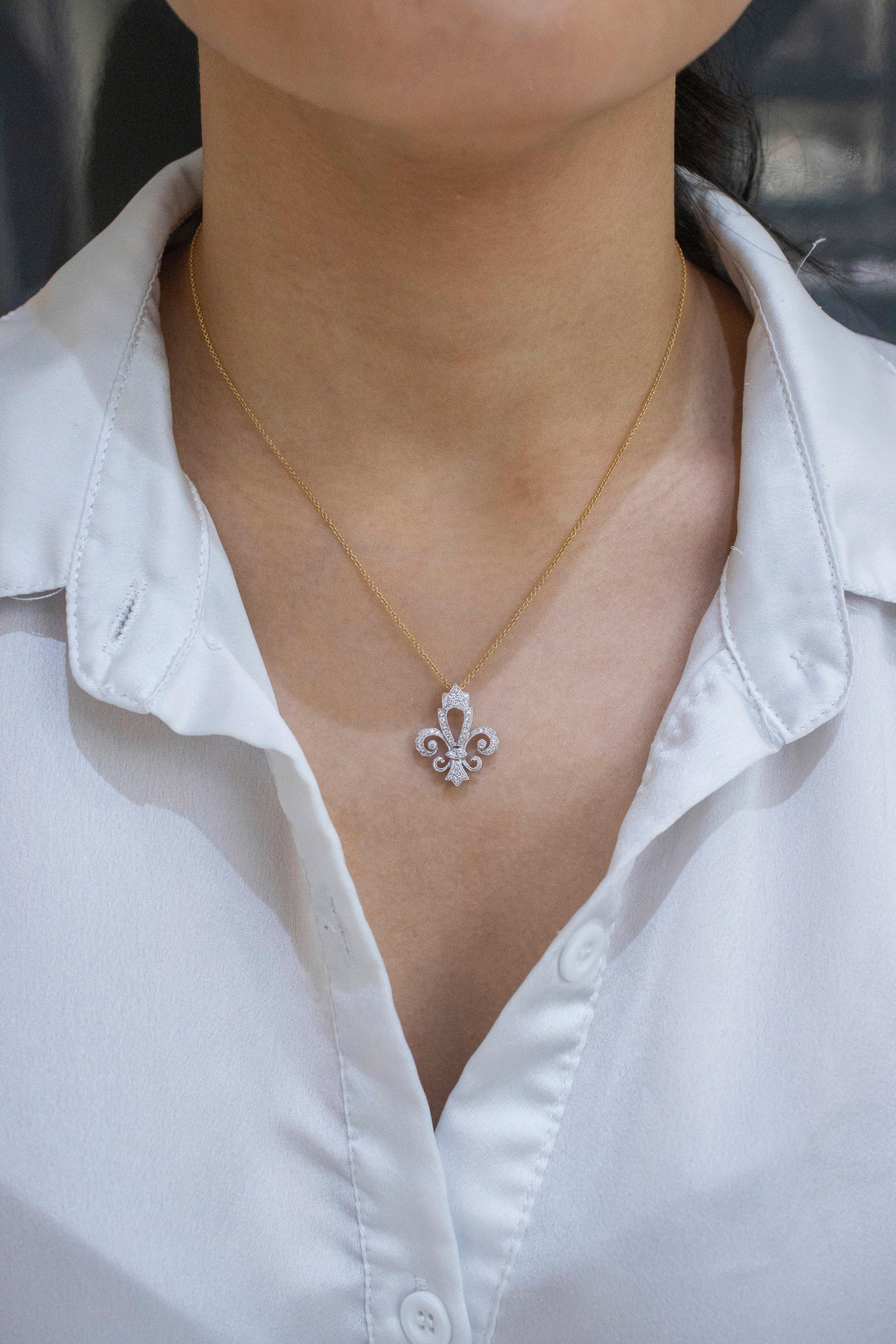 A fashionable pendant showcasing round brilliant diamonds, set in a fleur-de-lis design made in 18 karat white gold. Diamonds weigh 0.23 carats total. Suspended on a yellow gold chain.


