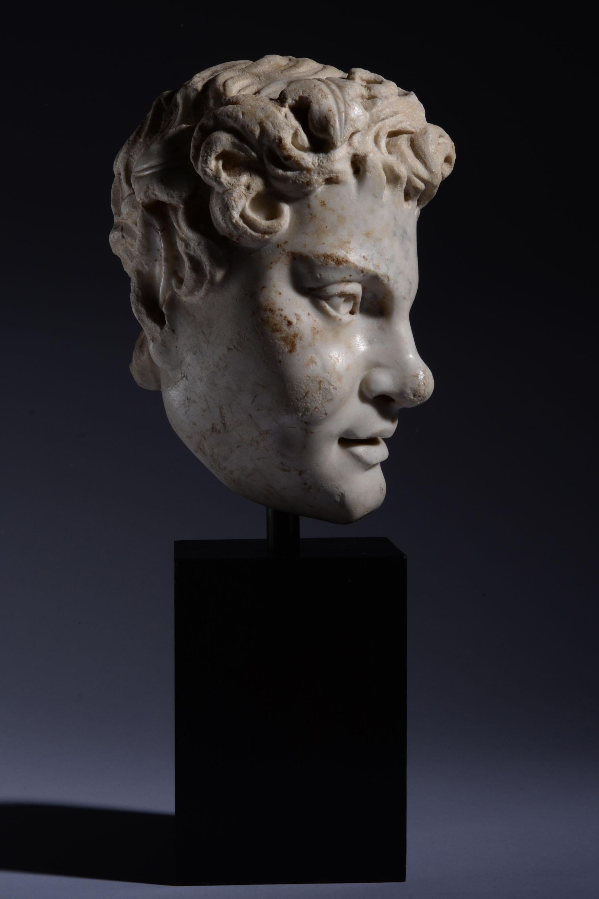 Tête de satyre
Romaine, vers le IIe - IIIe siècle ADS 
Marbre sculpté et hautement poli

Tête de satyre en marbre extrêmement fine, représentée avec une couronne de lierre, des cheveux bouclés et une oreille de chèvre pointue. Les lèvres pleines