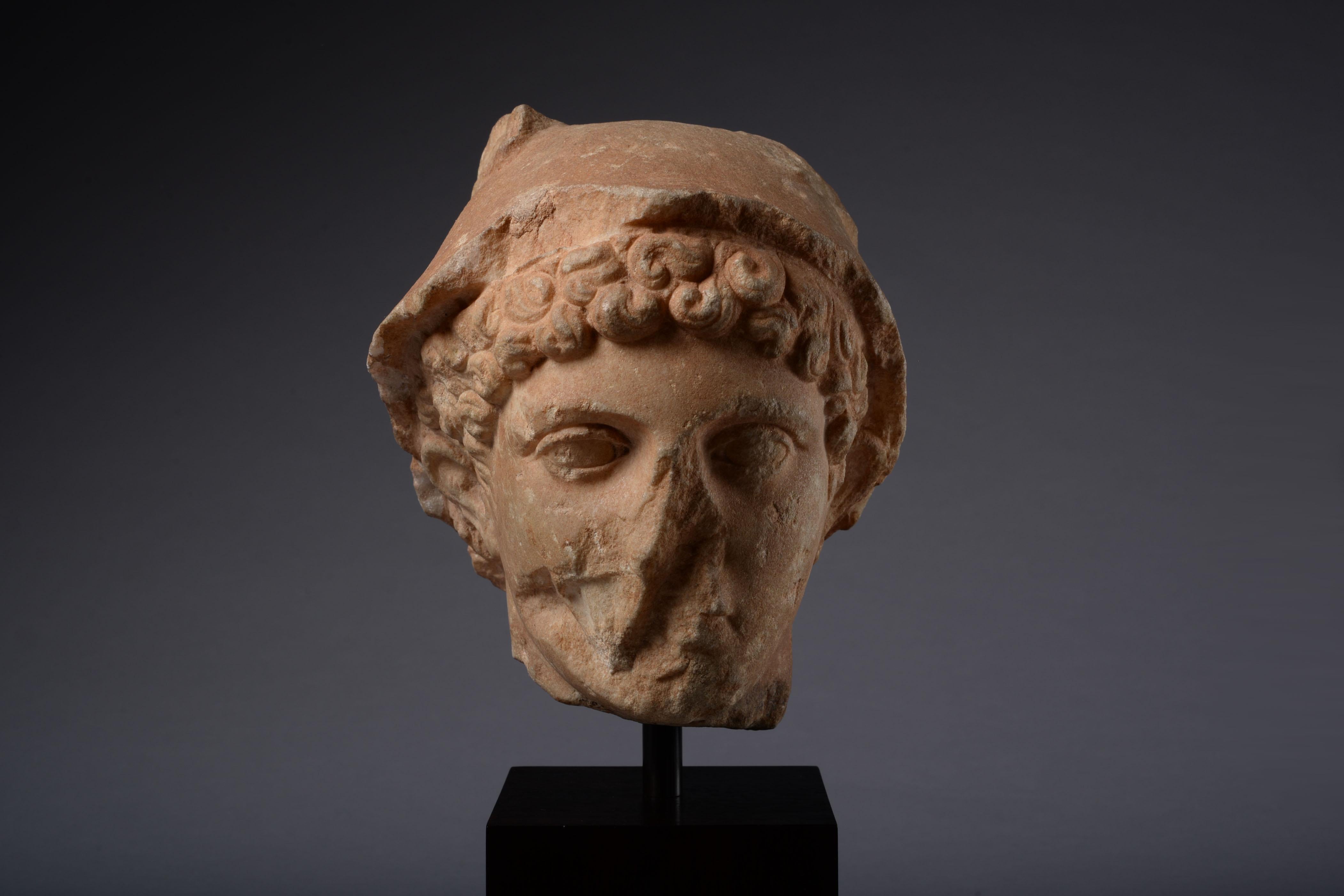 Roman marble head of Mercury, 'the divine trickster', circa 1st-2nd century AD.

With deep-set, almond-shaped eyes and rows of short, thick, curls emerging from underneath the god's distinctive winged petasus sun hat.

Provenance:

From the