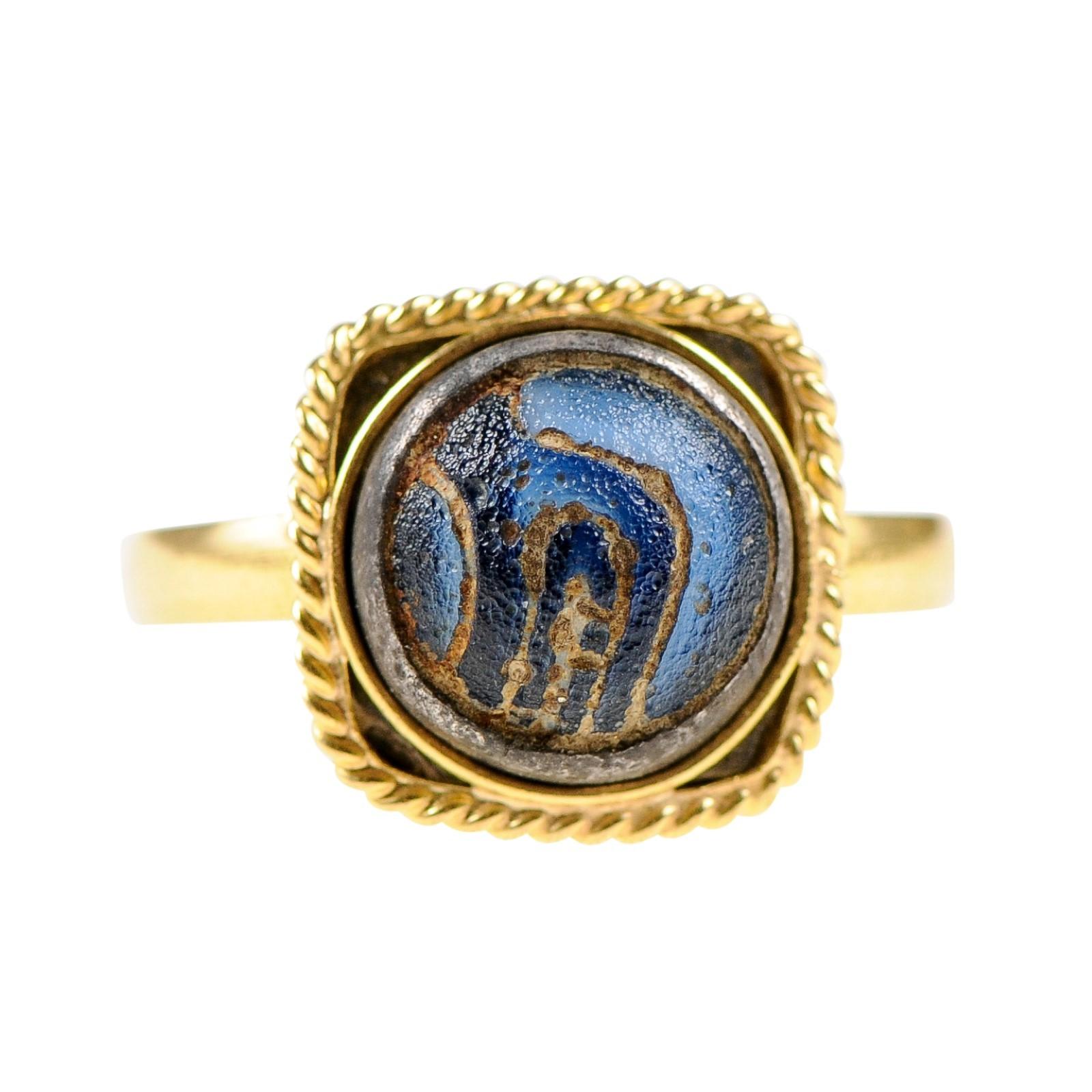 An authentic ancient Roman mosaic glass (4th to 6th century AD) custom mounted within a 21k gold band and squared/rope bezel. The coloration of this ancient Roman glass is cobalt/navy blue in color, with beautiful engraving, which contrasts nicely