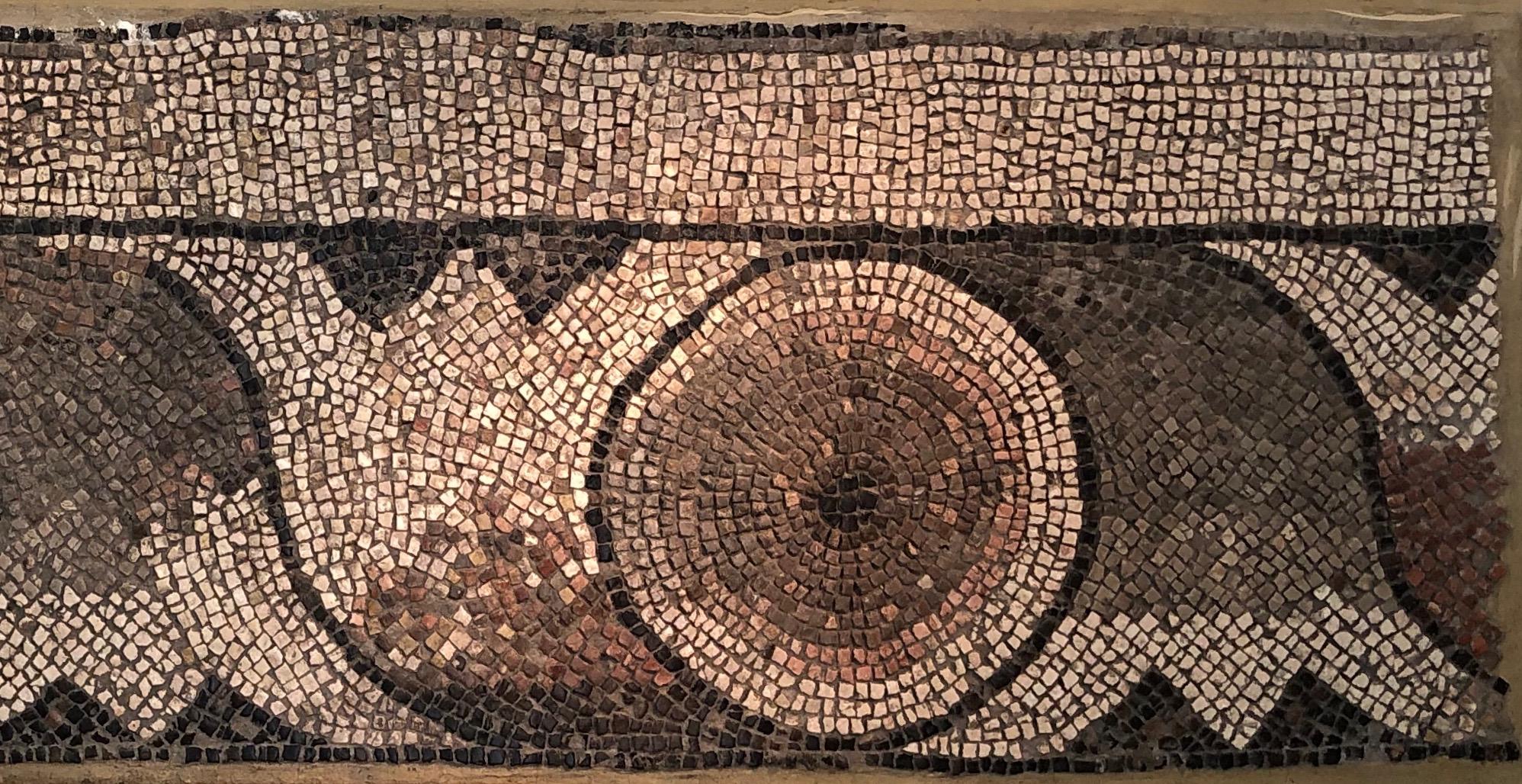 This late Roman, circa 4th-5th century AD mosaic designed with a wavy lotus flower motive, is made of small stones or marble squares of different colors, called tesserae, that are posed upon a bed of cement that is framed by a metal (brass)