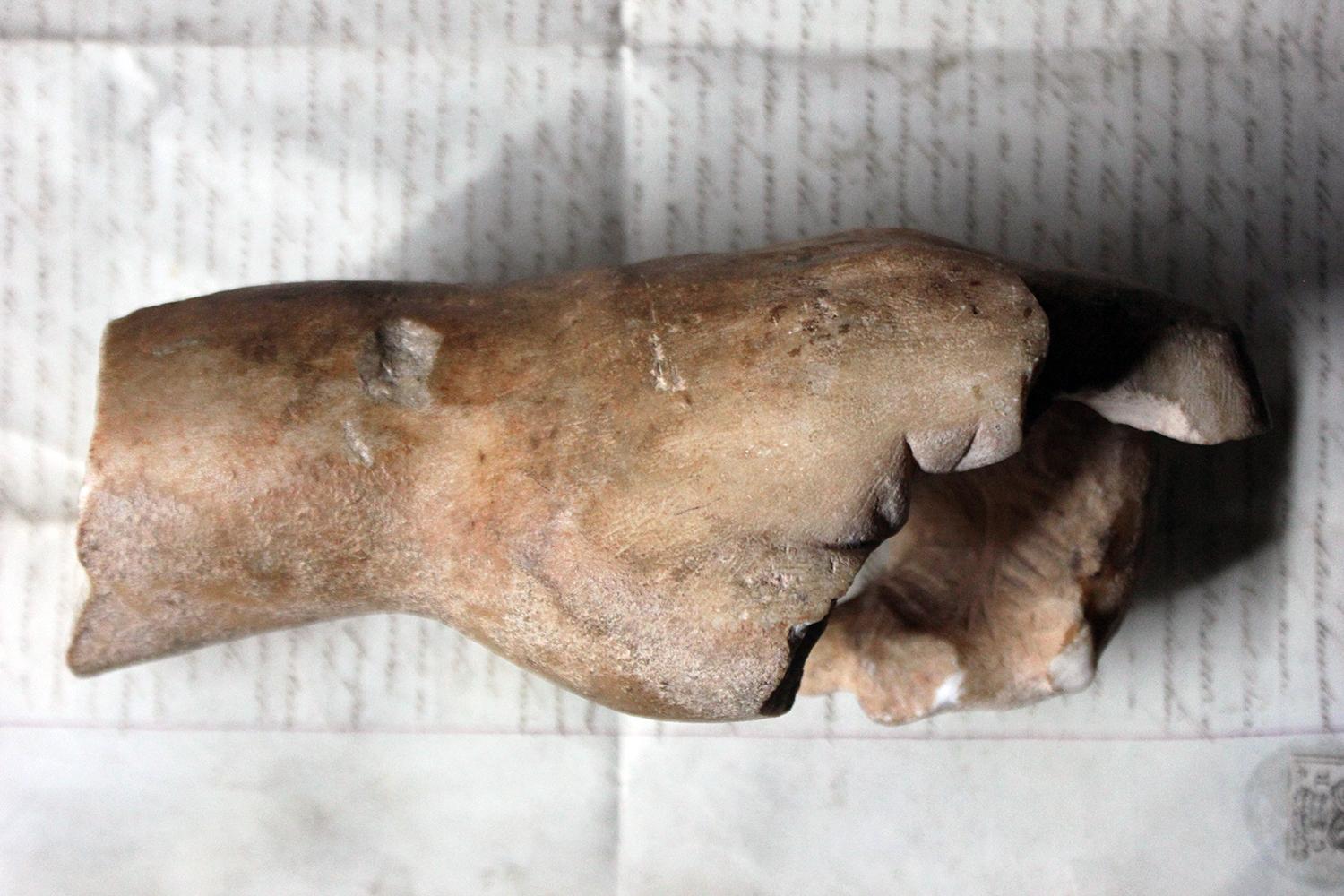 The weathered marble fragmentary hand, of oversized proportions, with coiled fingers once holding an attribute, the marble having a good patination, and surviving from the late 1st century AD period.

The hand has several losses, and repairs, as